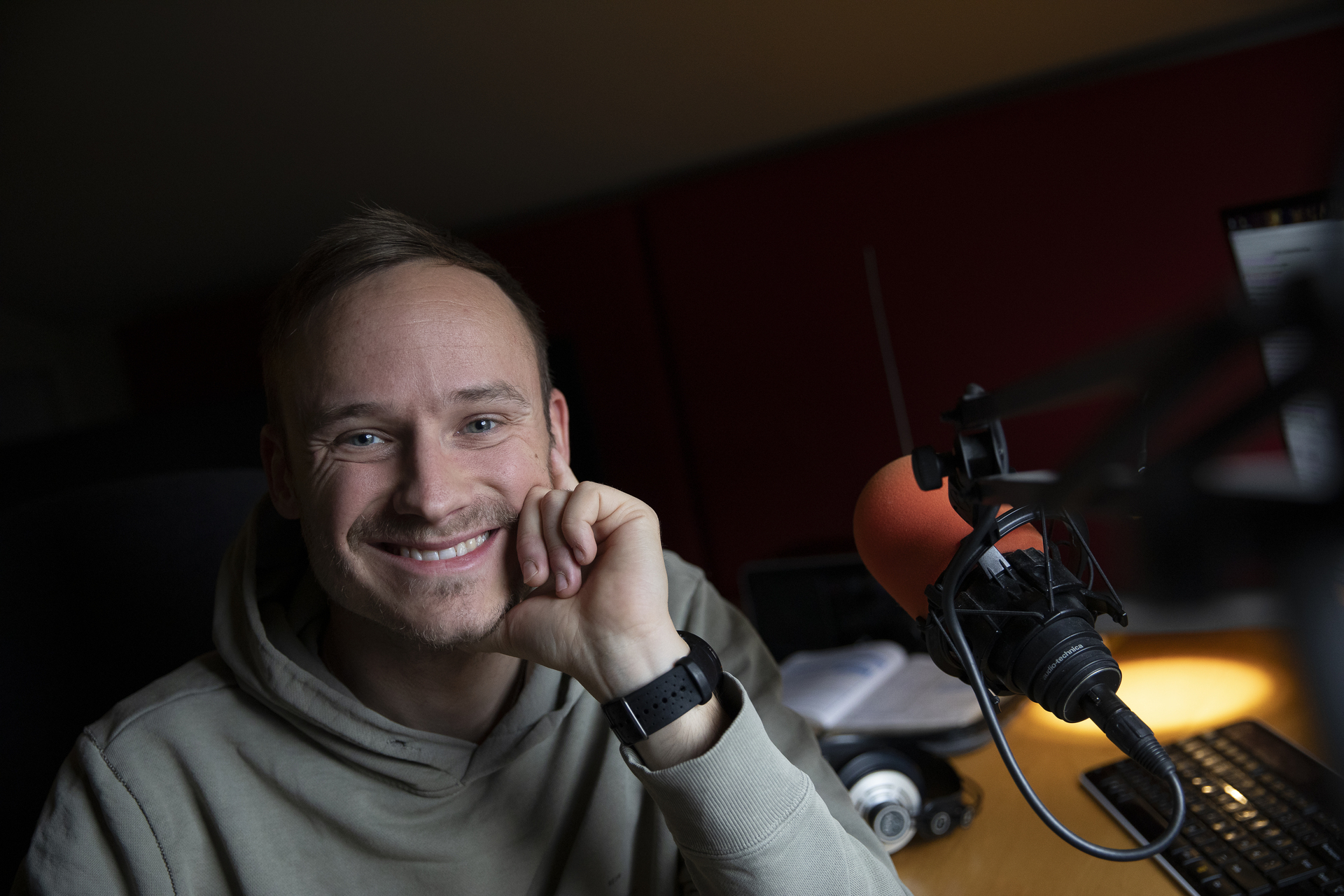 Ung mann med skjegg smiler ved siden av en mikrofon