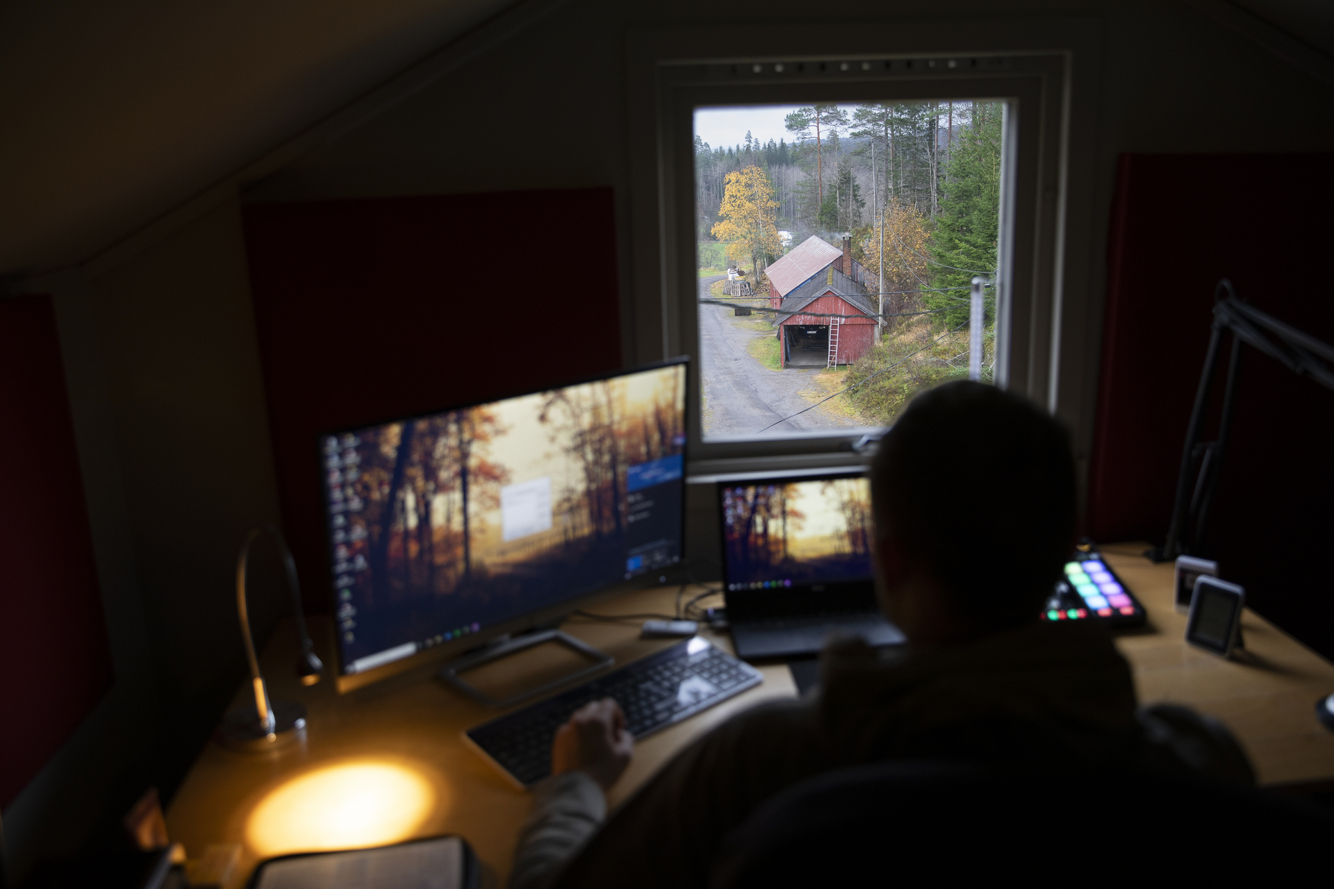 Mann sitter foran en skjerm i et studio og ser ut på gårdsbygninger utenfor vinduet