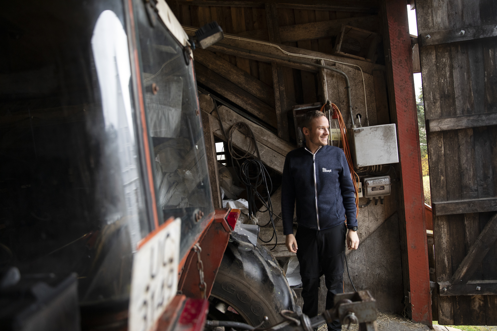 Ung mann står inne i en låve med en traktor i forgrunnen.