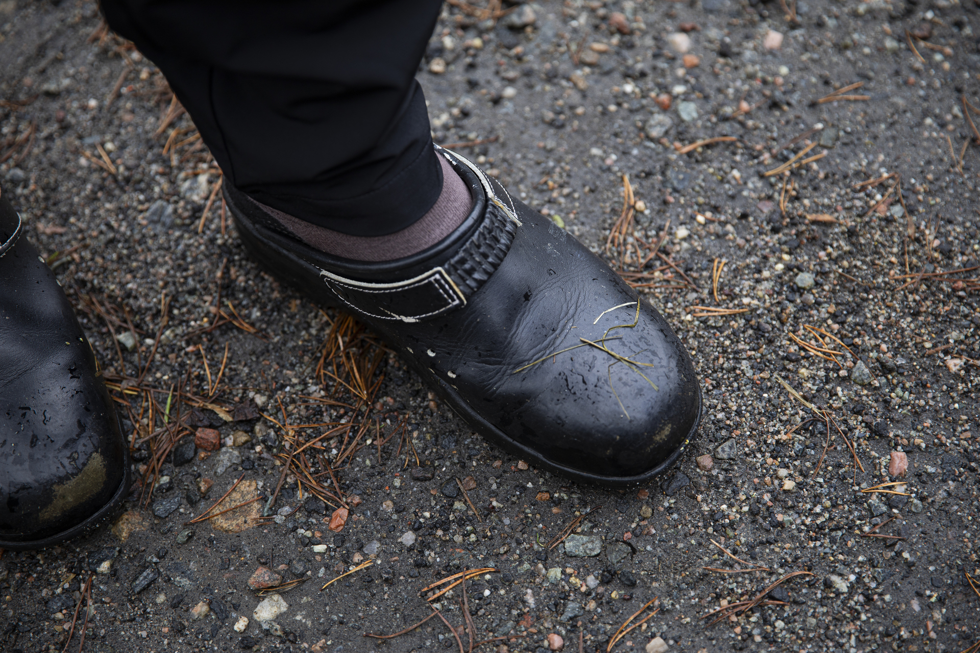 Bein med sorte tresko på. Litt gress og rusk oppå skotuppene.