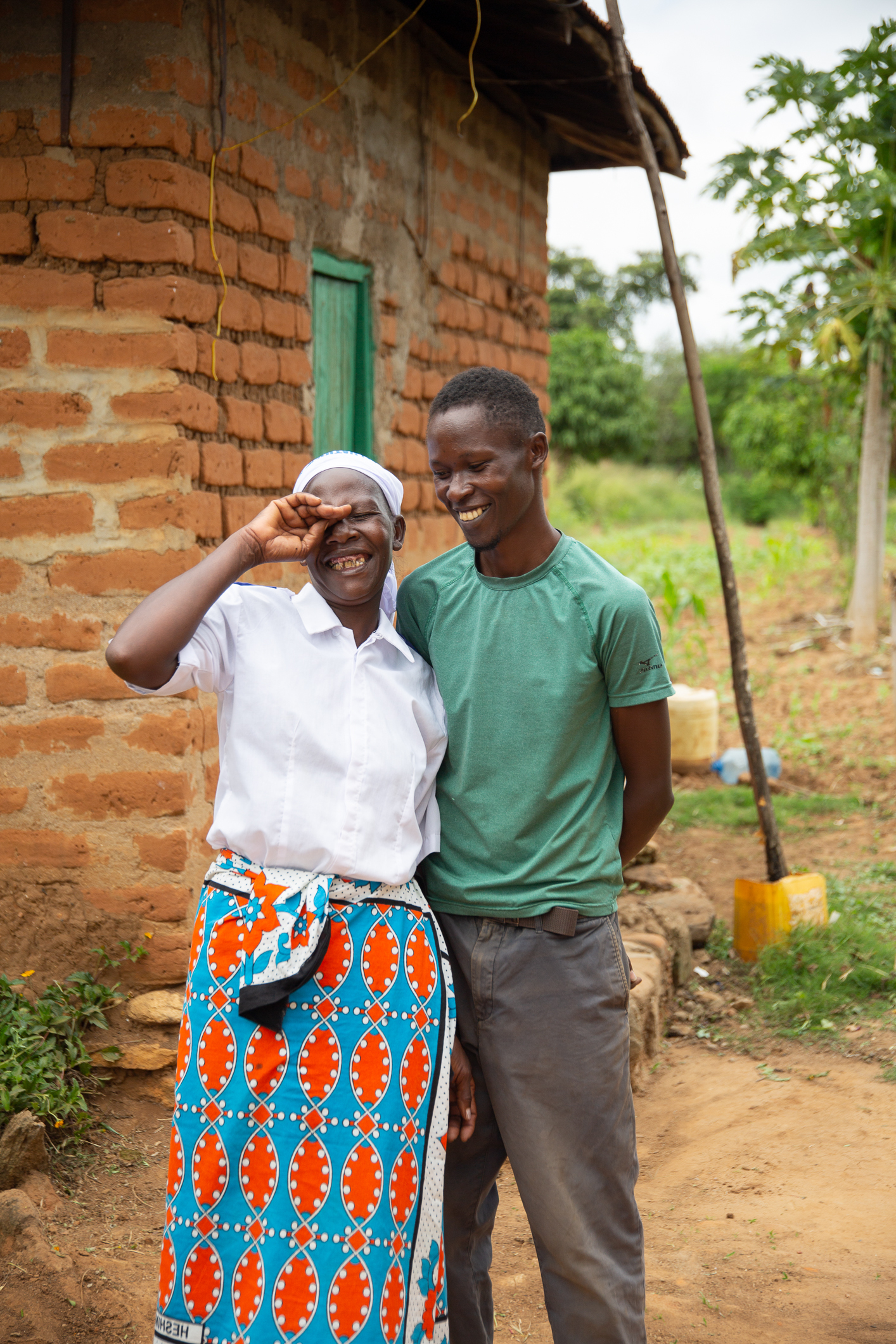 Mor og voksen sønn står utendørs med naturlandskap i bakgrunnen