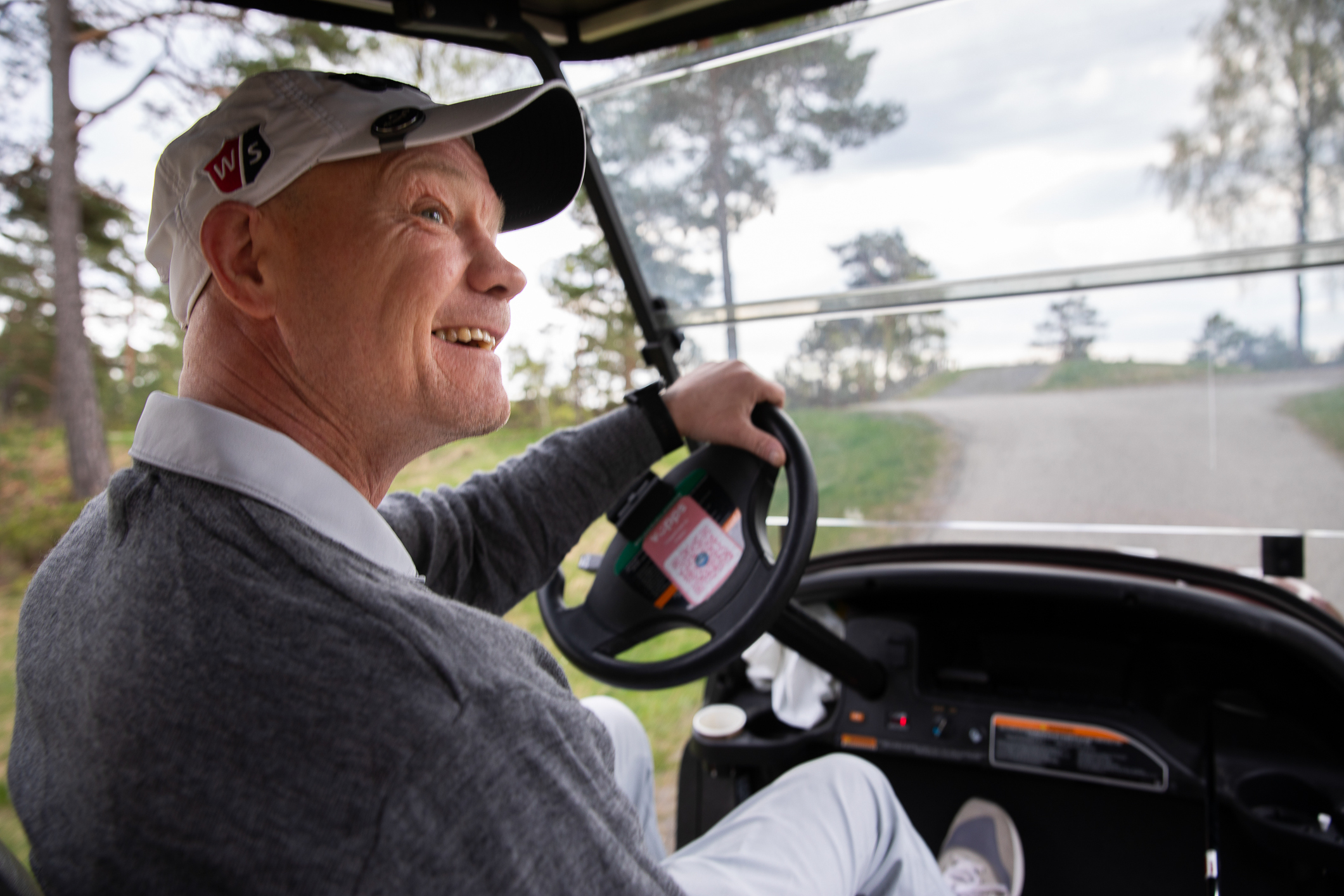 Foto: To bilder etter hverandre. Det først viser en smilende mann med caps som kjører en golfbil. Bildet er tatt innefra, slik at en ser ut på grusveien gjennom ruta. Det andre bildet viser en hånd som holder opp en golfkølle med et spesielt grep.