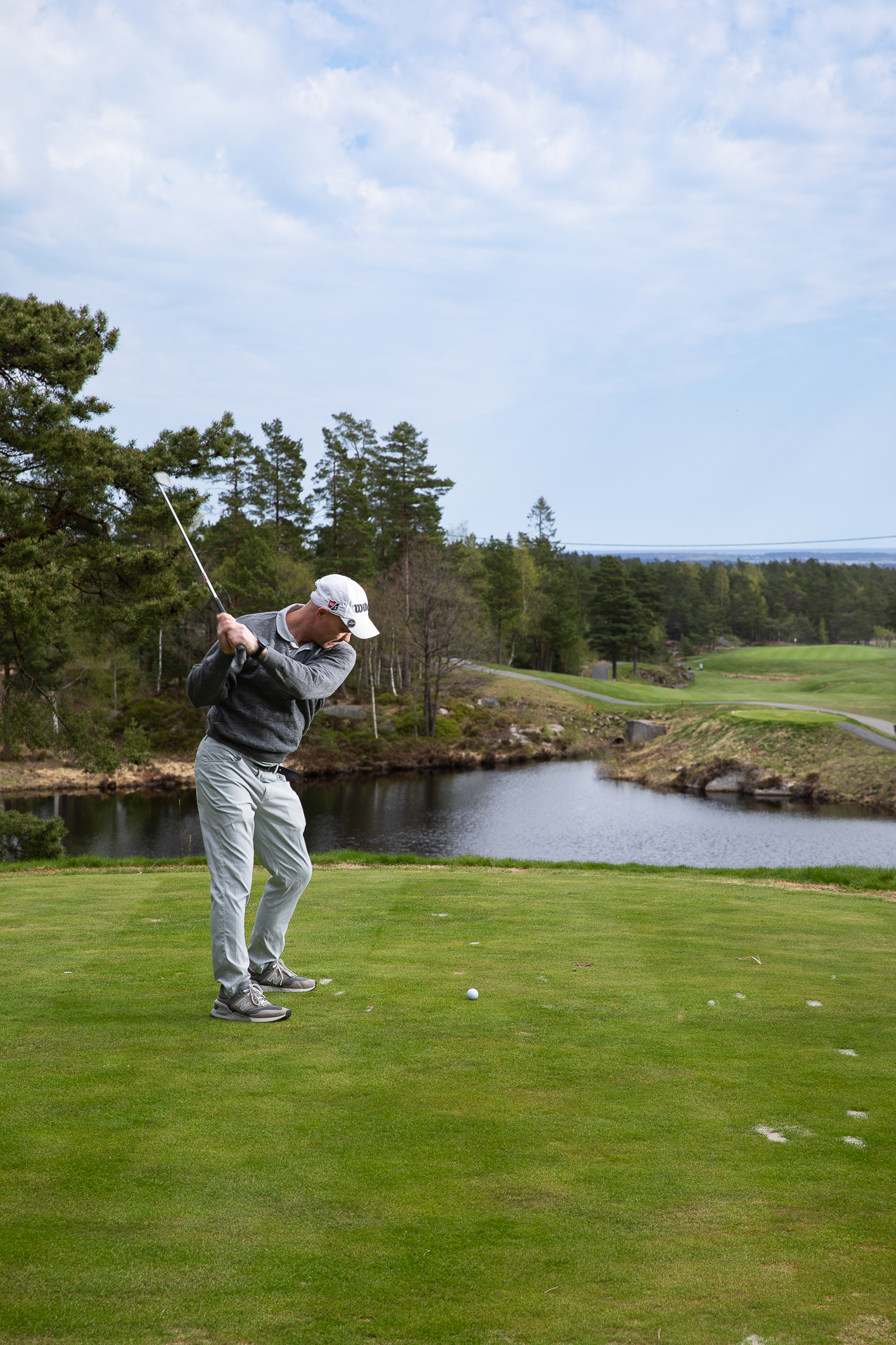 Foto: Mann i golfklær svinger kølla og skal til å slå golfballen.