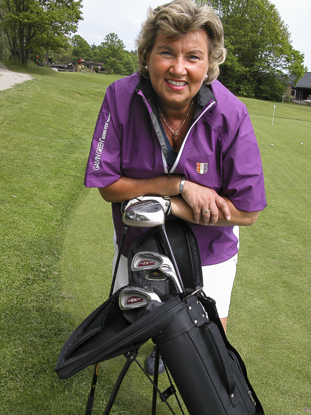 Foto: Godt voksen kvinne i golfklær lener seg over en golfbag med køller.