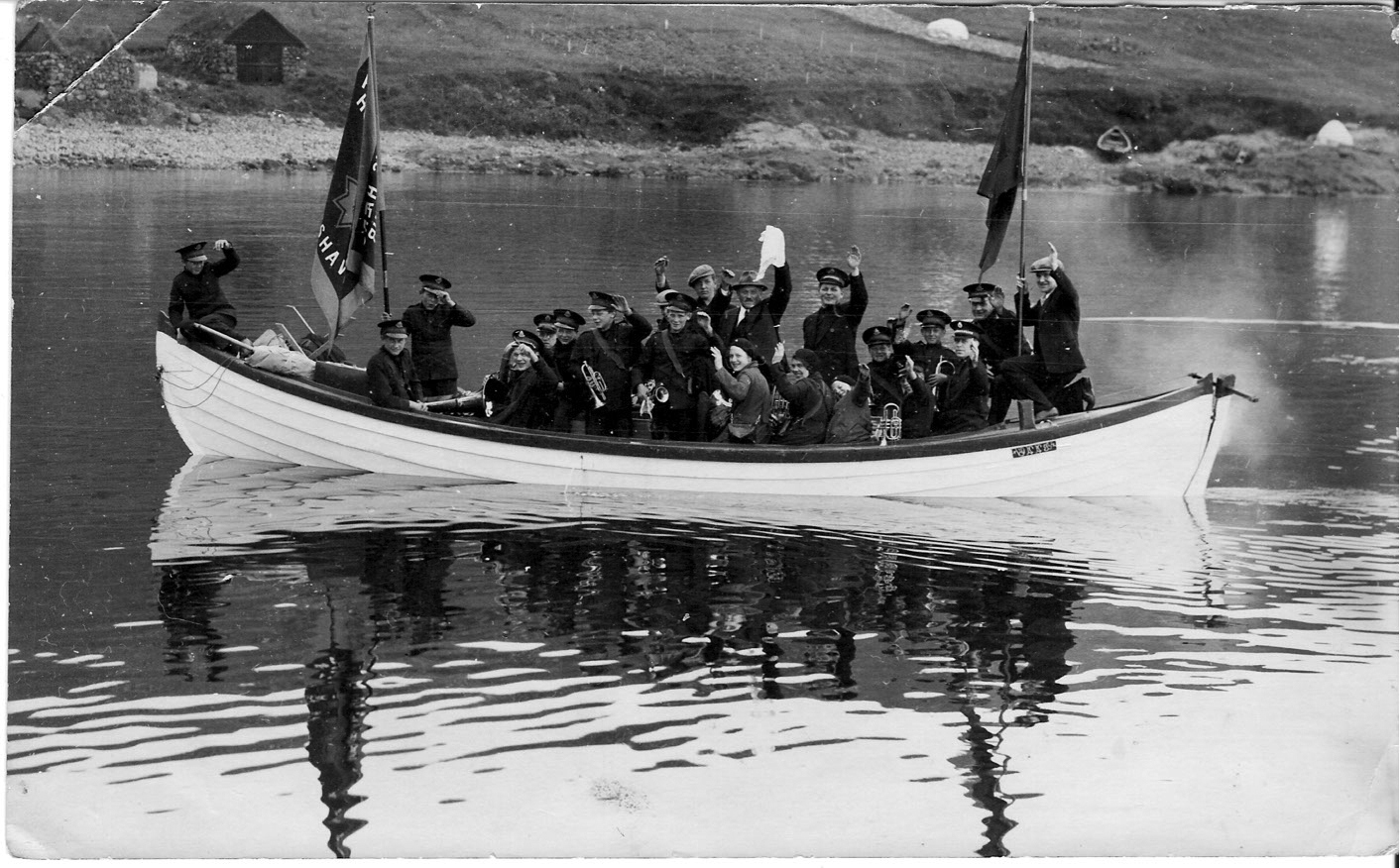 Foto: Svart-hvitt bilde av instrumenter og musikanter i uniform i en liten, åpen båt.