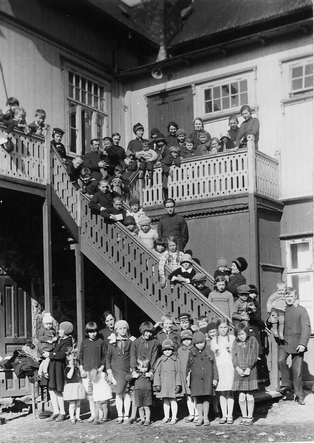 Foto: Svart-hvitt-bilde av barn som sitter i ei langt trapp til et gammelt hus.