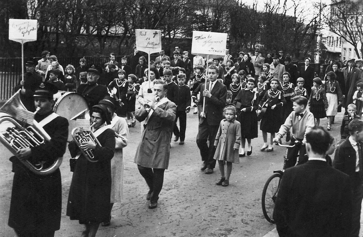 Foto: Svart-hvitt-bilde av folk korps som går foran et tog med mennesker.