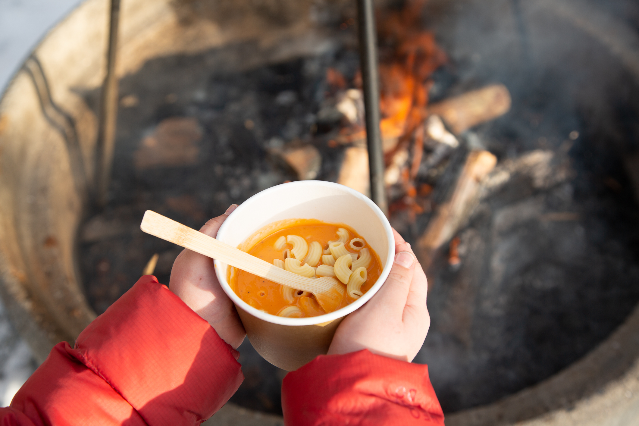Bente Eriksen, speiderleder, lager mat sammen med et av barna foran bålet.