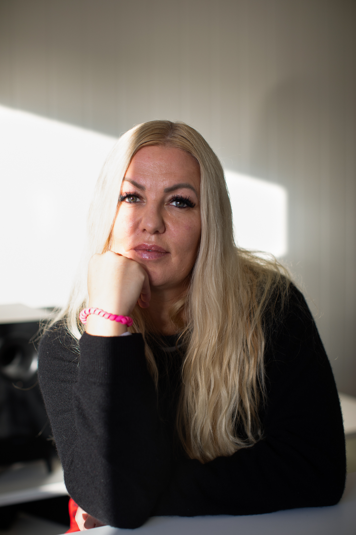 Foto: Dame med langt, blondt hår sitter med albuen på bordet. Ser inn i kamera.