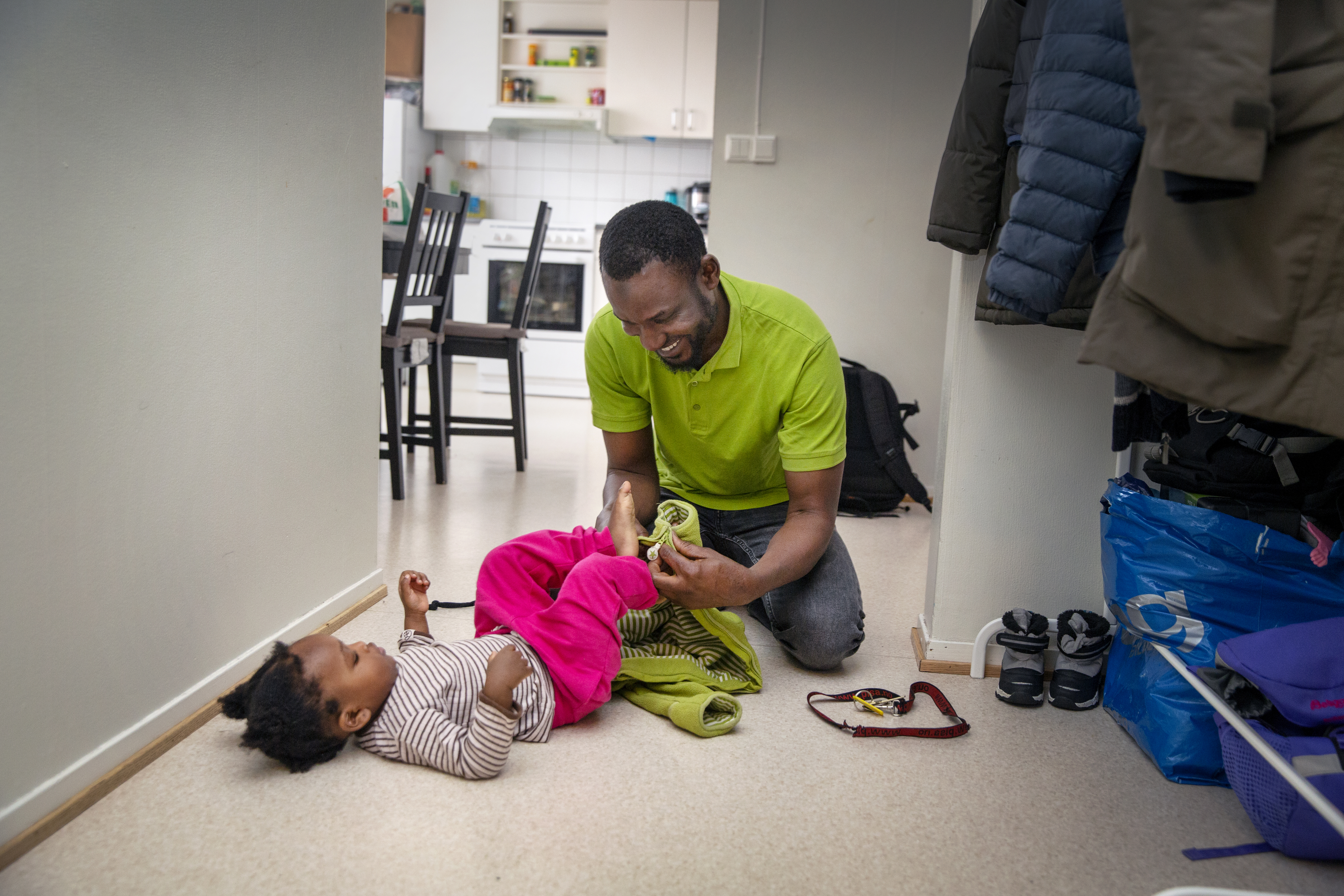 en far som hjelper en datter, som ligger på gulvet, på med utedressen