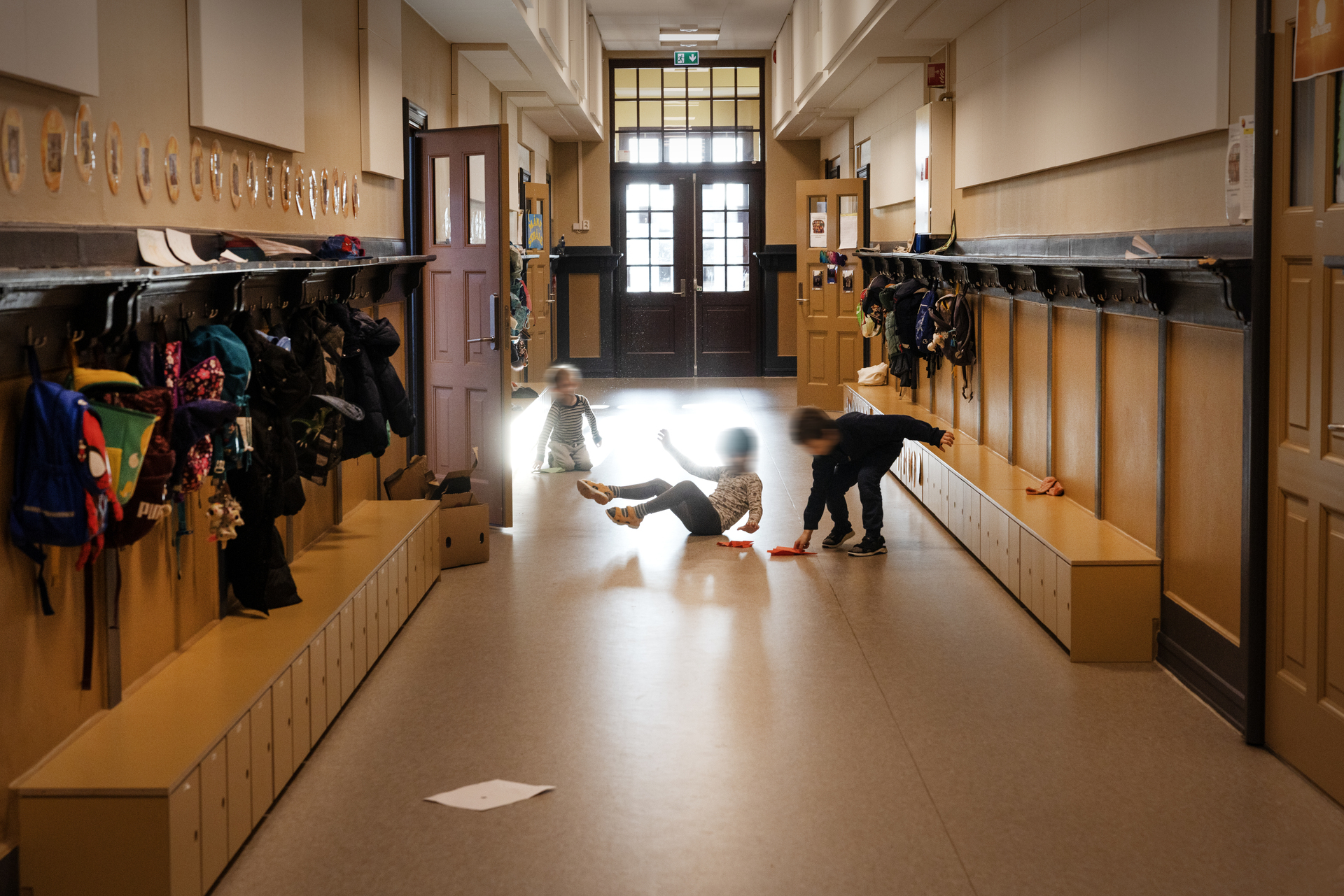 Foto: Tre små barn leker i en nyoppusset garderobe i en lang korridor i gammelt bygg.