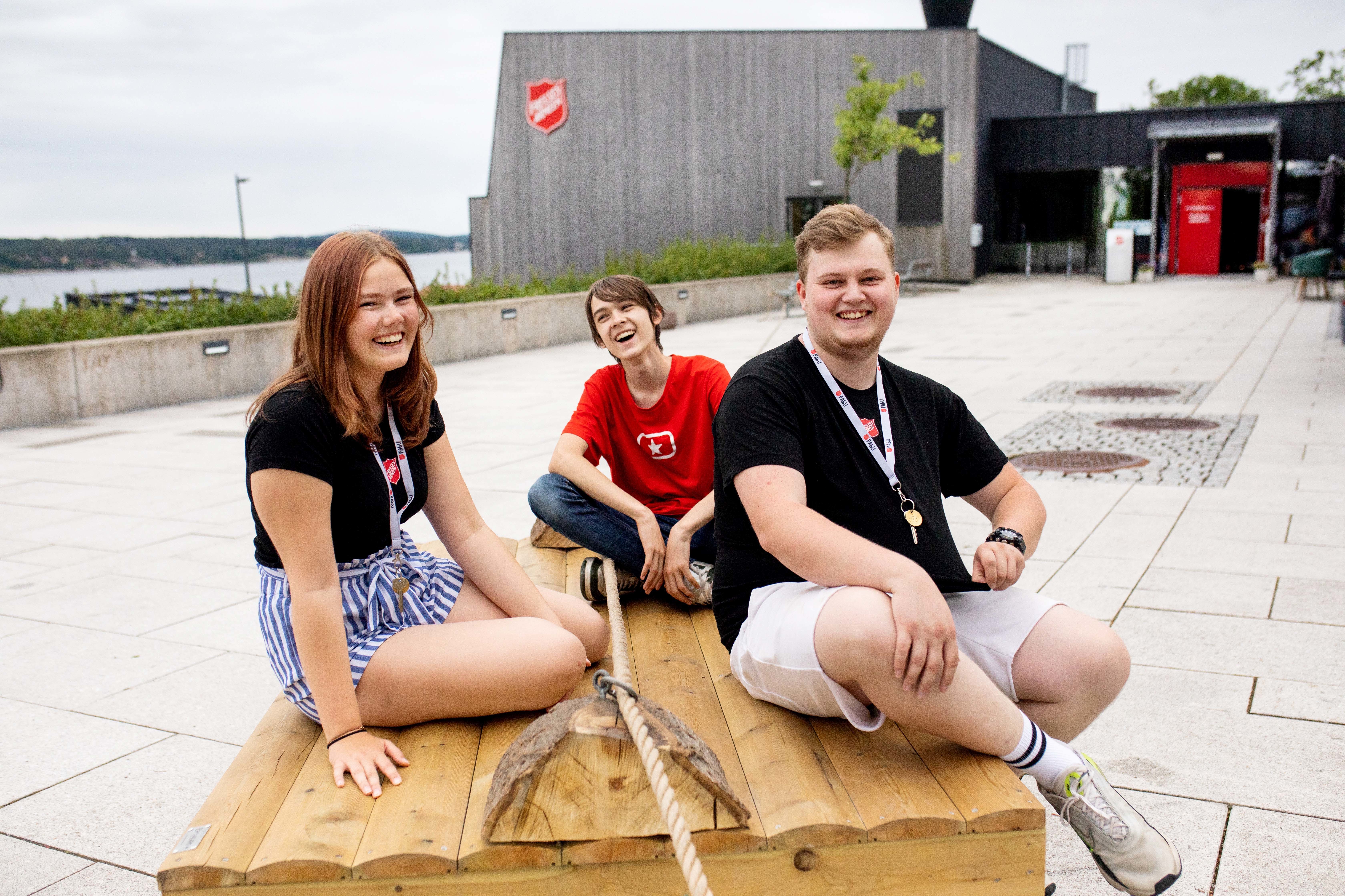 Tre unge ledere sitter på et bord foran FA kurssenter på Jeløy. De hjelper til med lek og moro for barna.