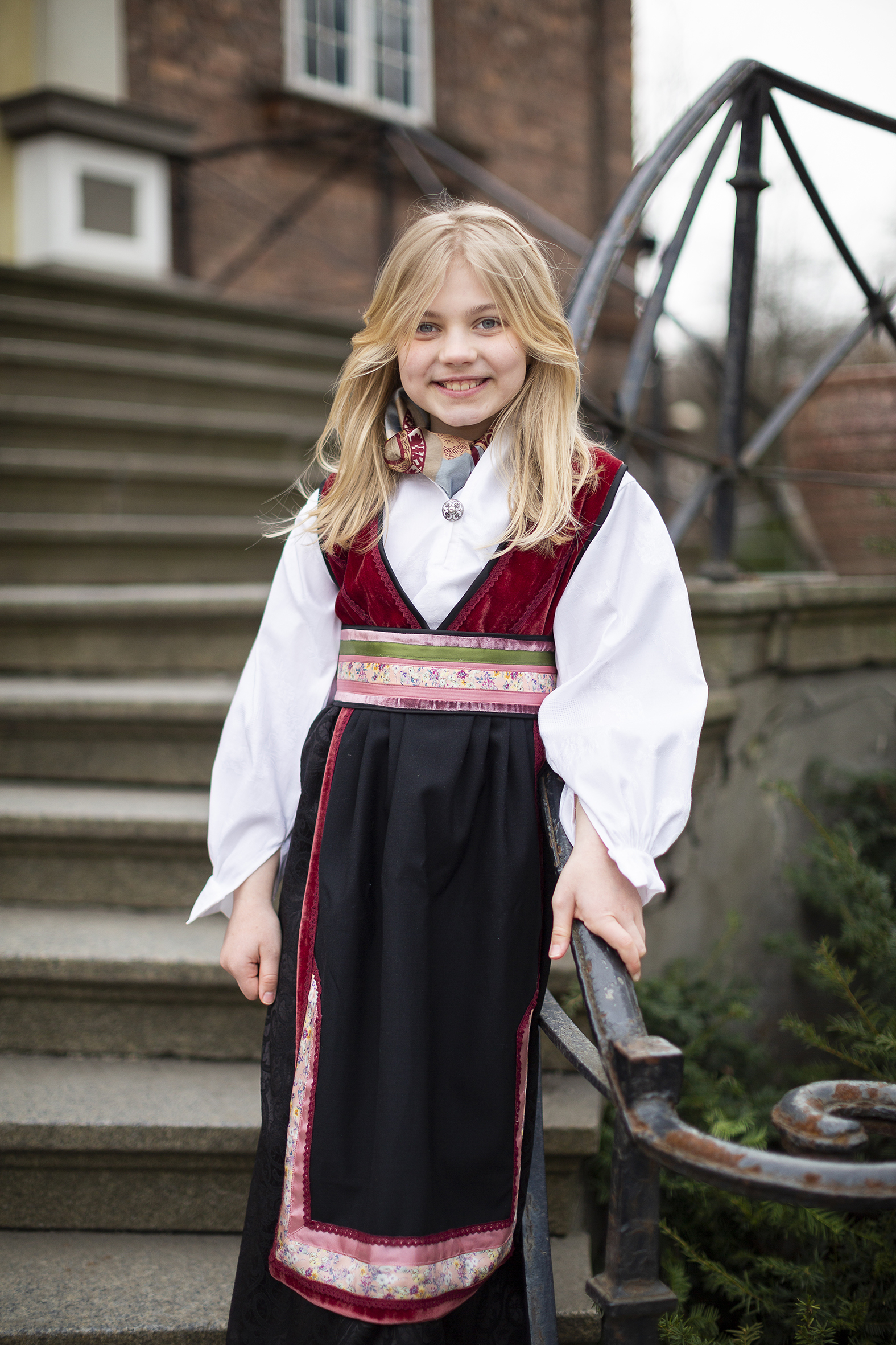 En jente på 9 år poserer på en kirketrapp i en fantasibunad sydd av Jobben