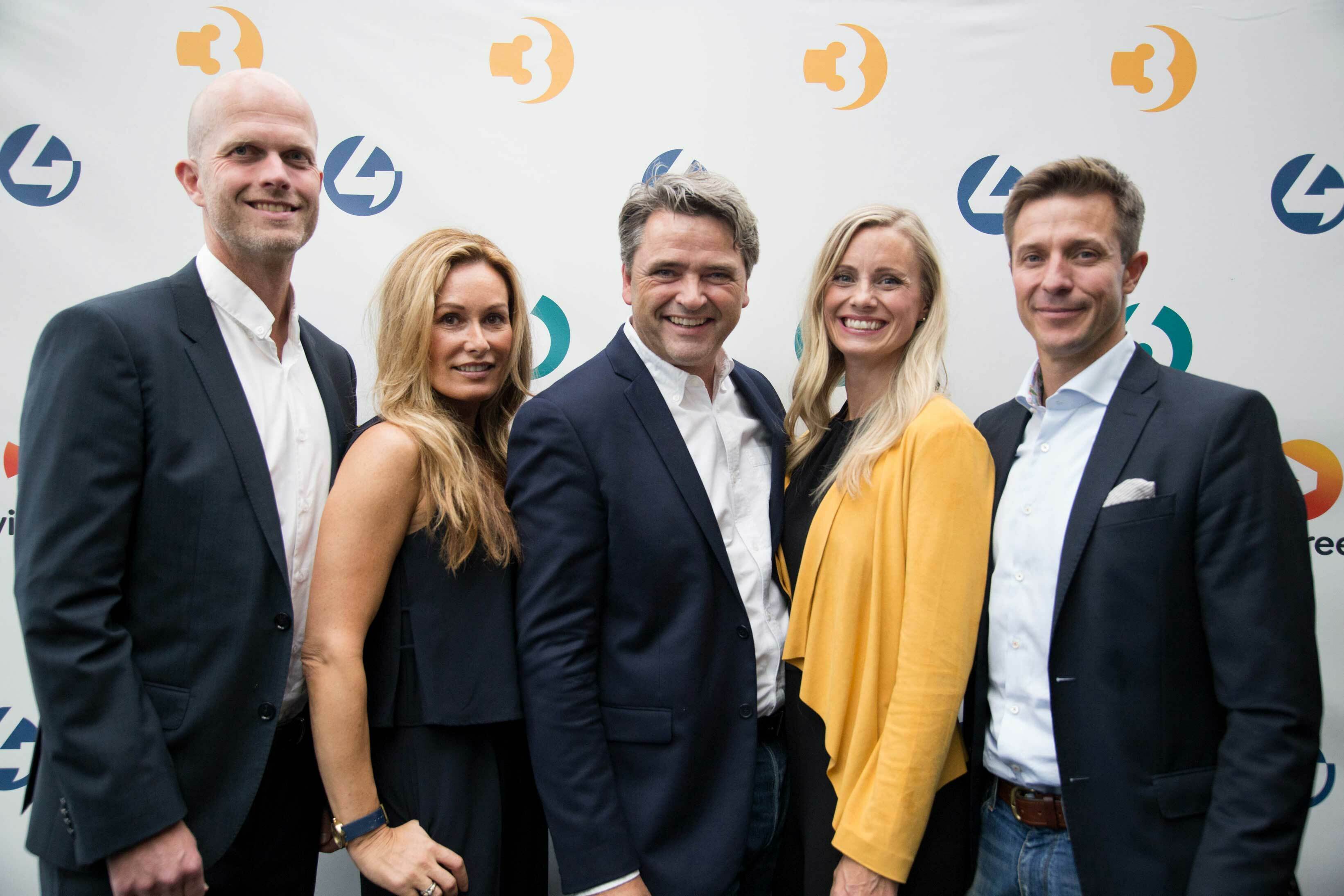 To kvinner og tre menn foran en vegg med TV-logoer.