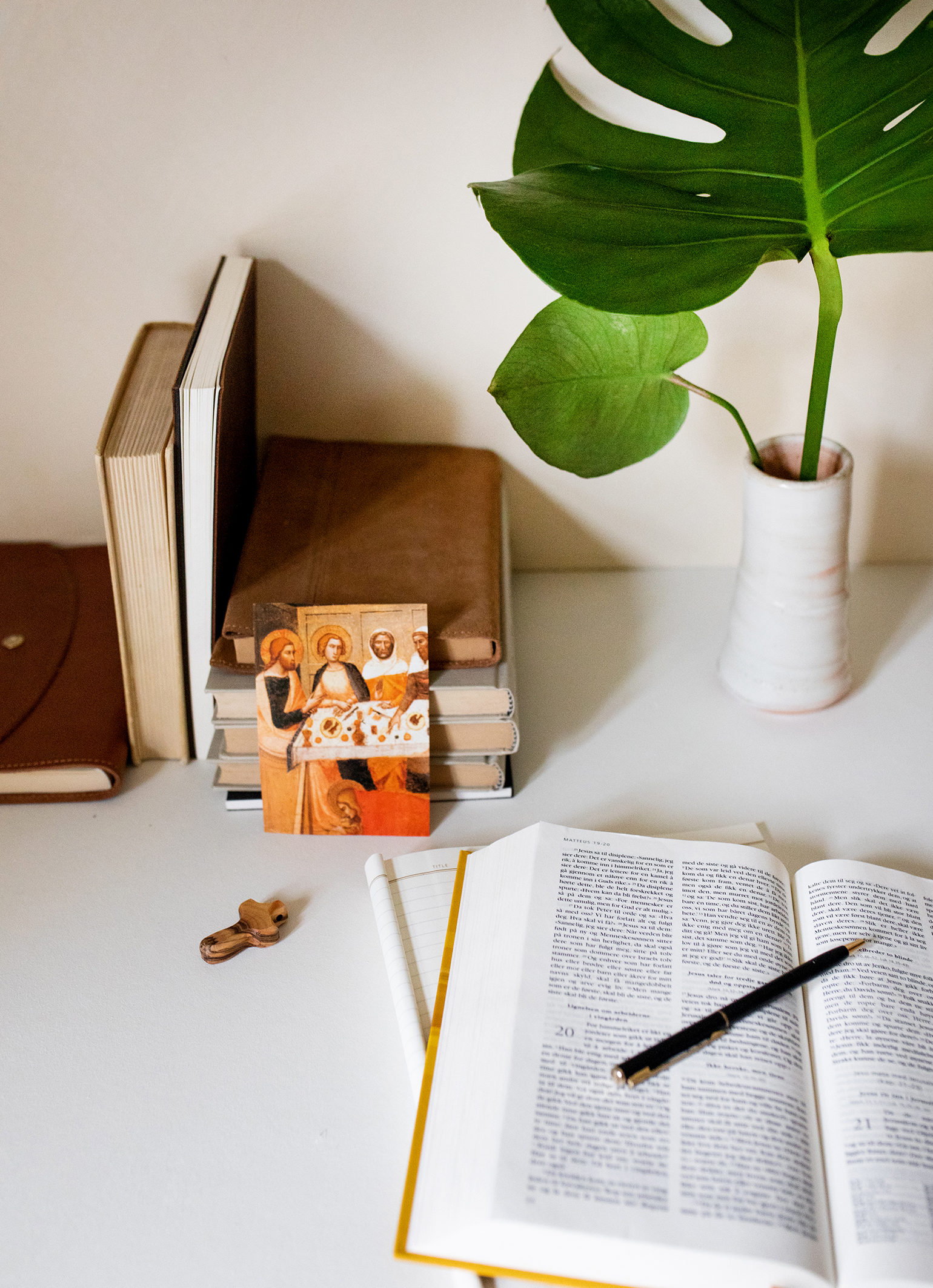 Bilde av gamle bøker, en oppslått bibel, et lite tre kors, noen grønne blader i en hvit vase og et kort som illustrerer disipplene som sitter å spiser