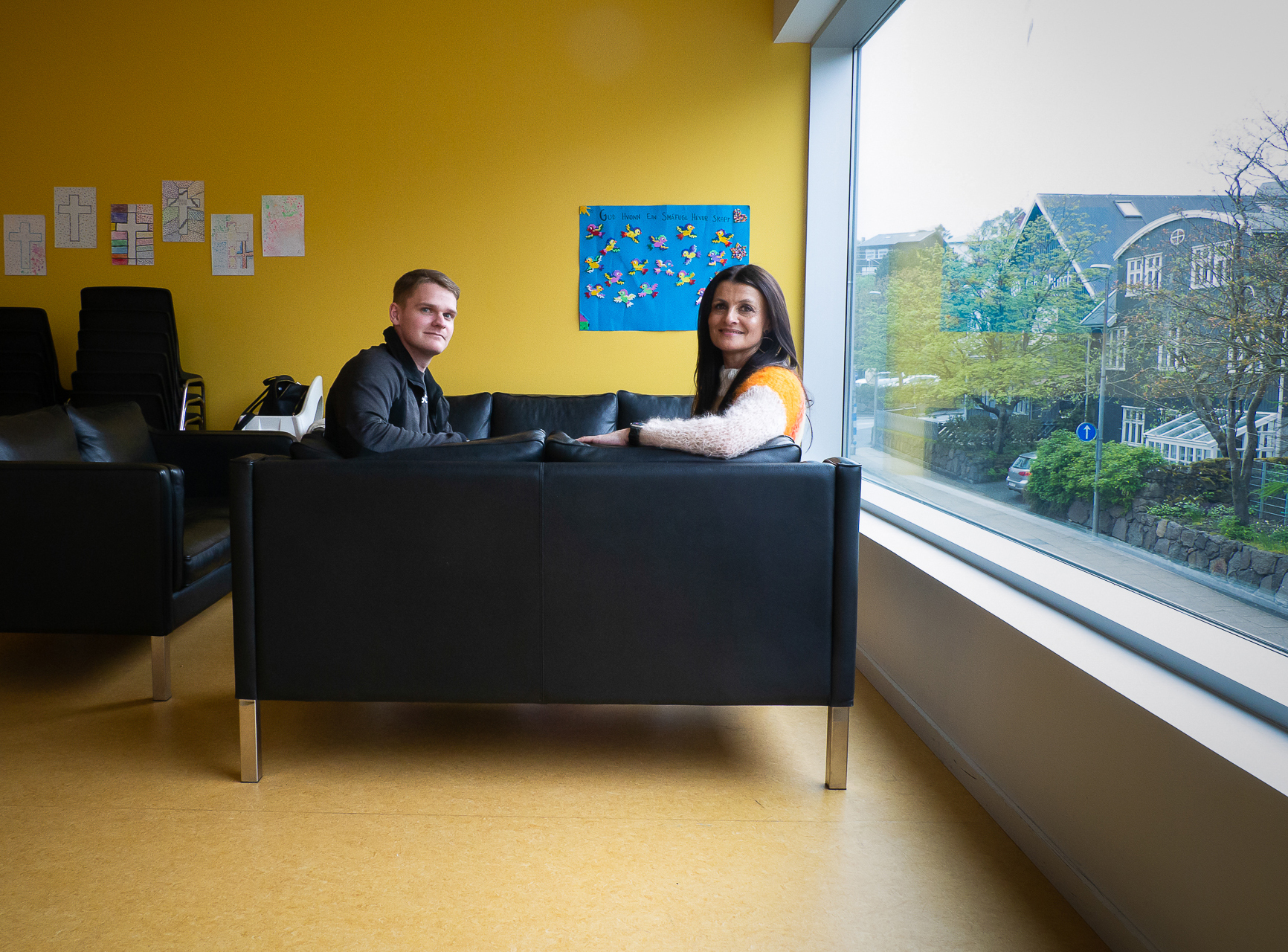 Ung mann og kvinne sitter i en skinnsofa som står med ryggen til. De to sitter vendt mot hverandre og snur seg slik at de begge ser i kamera.