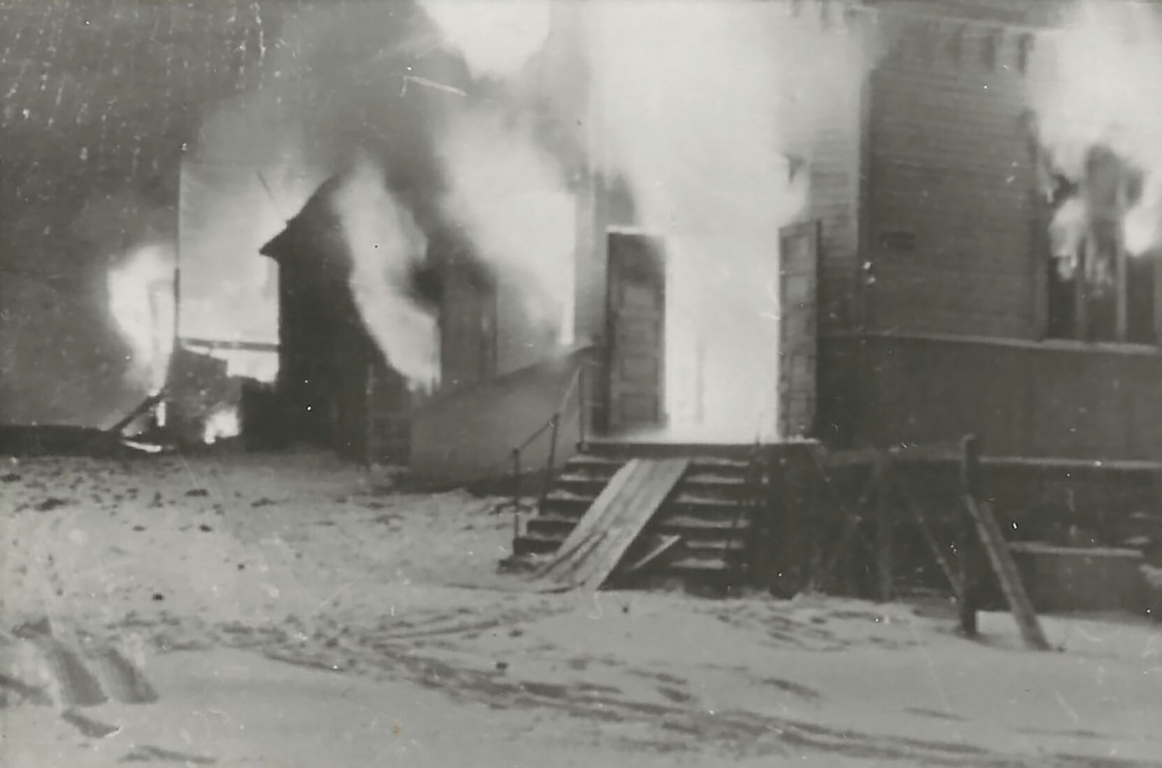 Foto: Gammelt svart-hvitt-bilde av hus som står i full brann. På bakken utenfor er det snø.