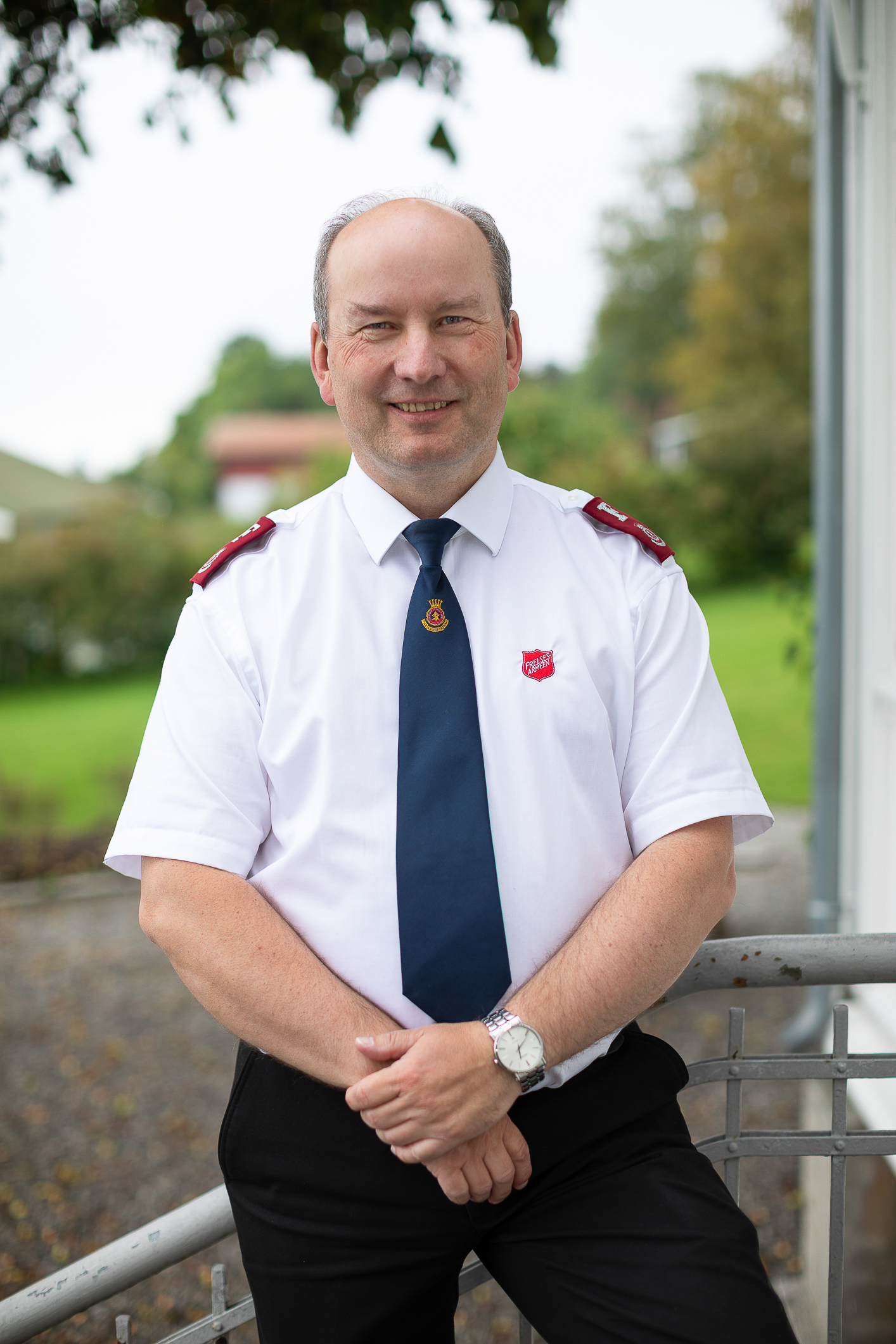 Mann i hvit skjorte og slips fra Frelsesarmeen poserer på trappa.