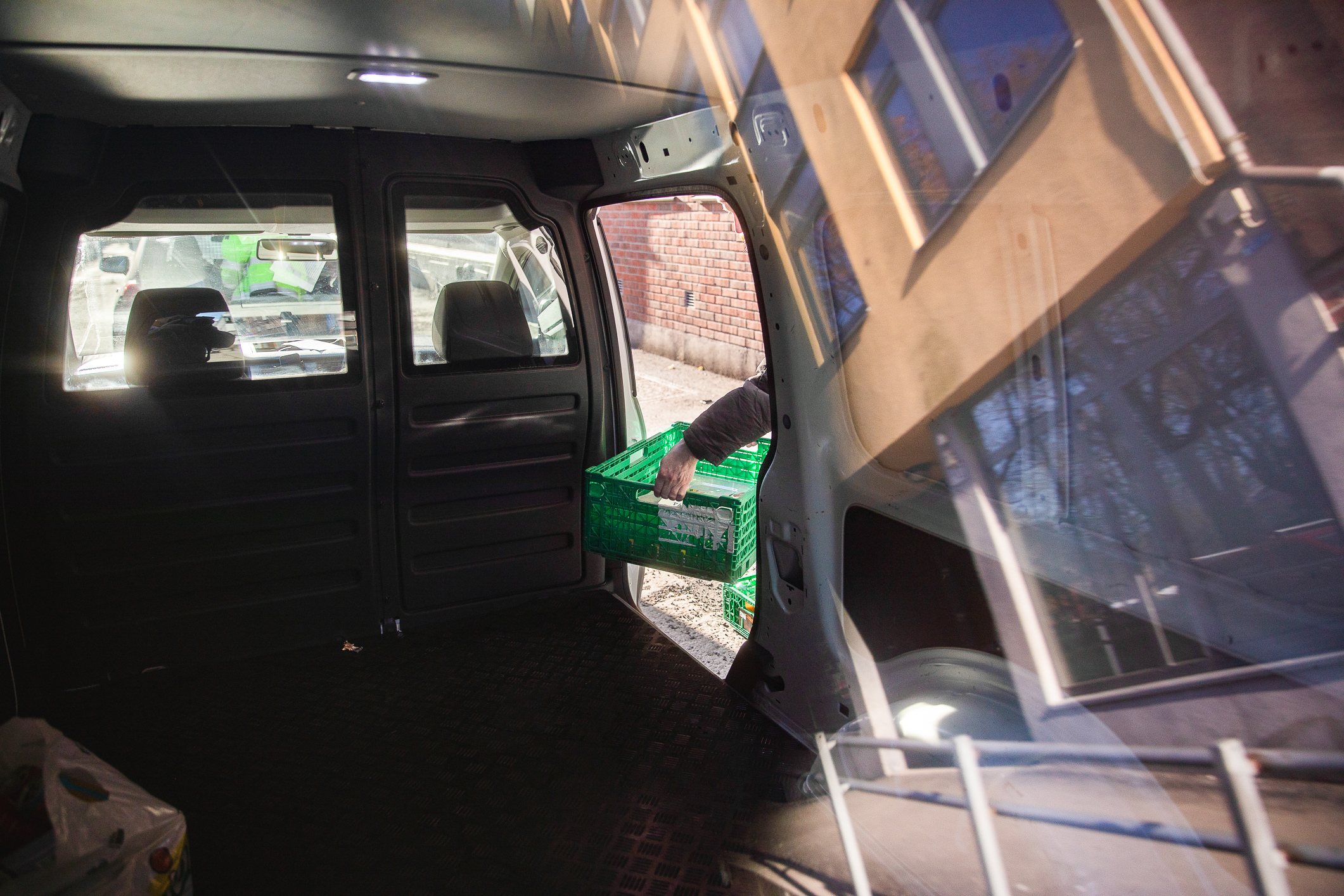 Foto: Innsiden av en kassebil. To hender løfter ut en grønn fruktkasse.