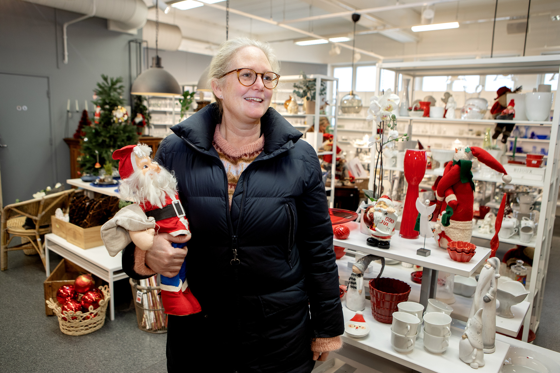 Kvinne i en julebutikk holder en nissefigur i armroken.