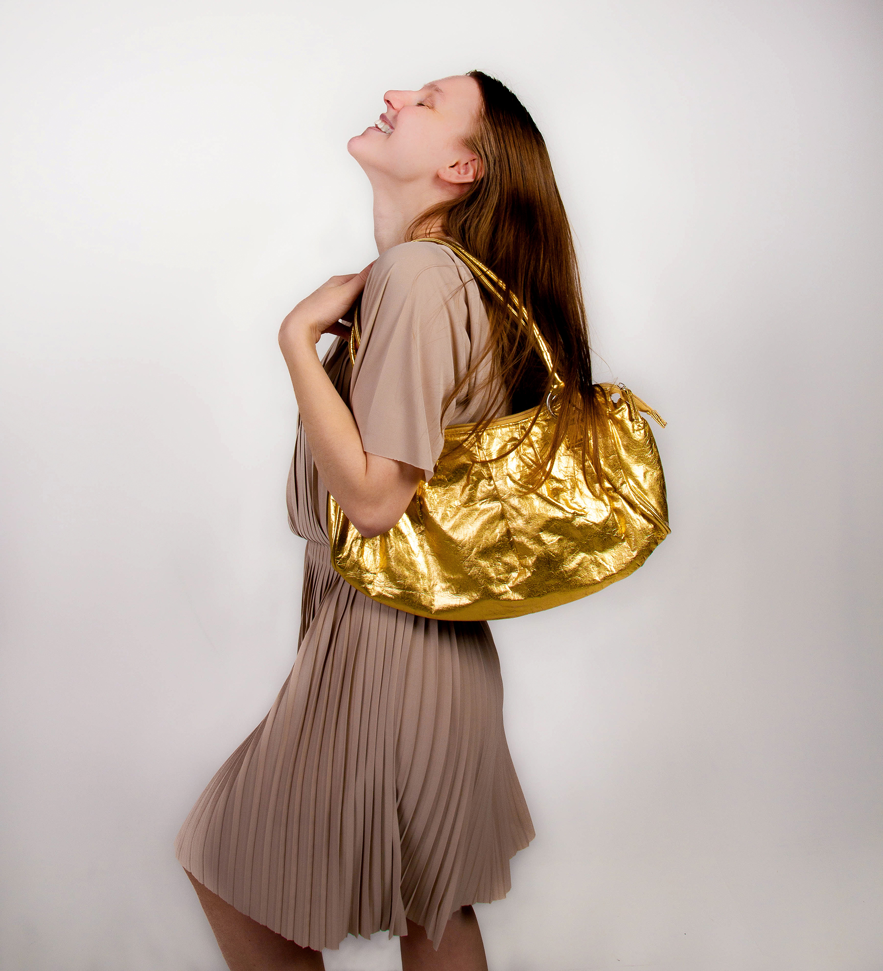 En jente i beige bluse og skjørt holder en gullfarget skulderveske og smiler