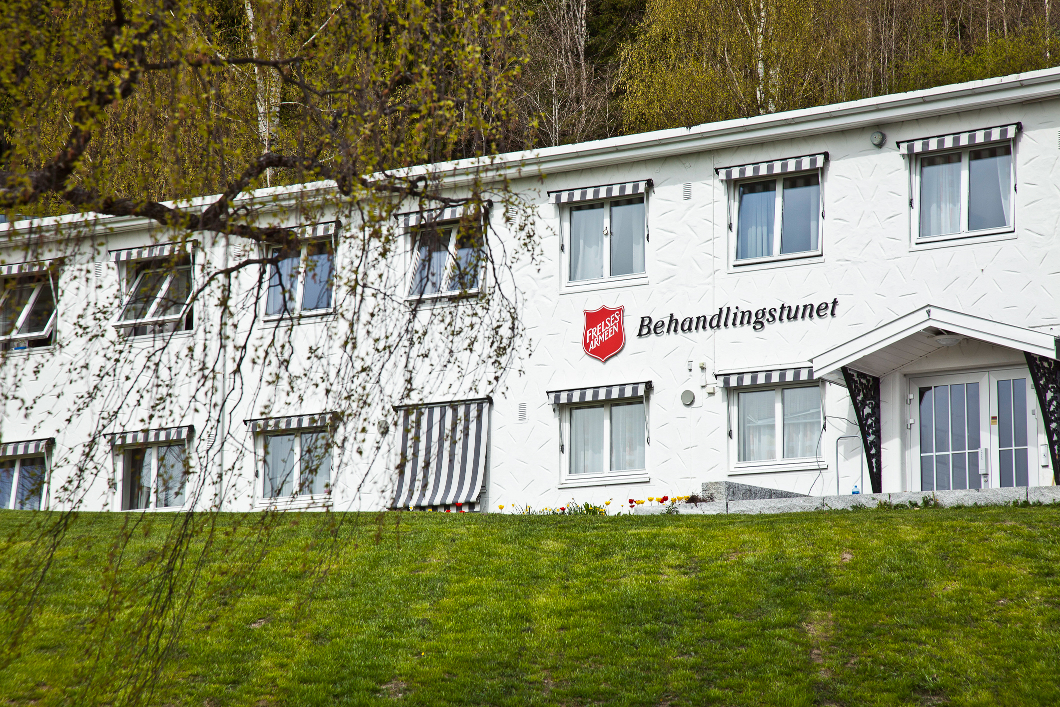 To bilder av samme bygg, der det ene er et bilde tett på og det andre viser skog, et par gårdshus og en hest i forgrunnen.