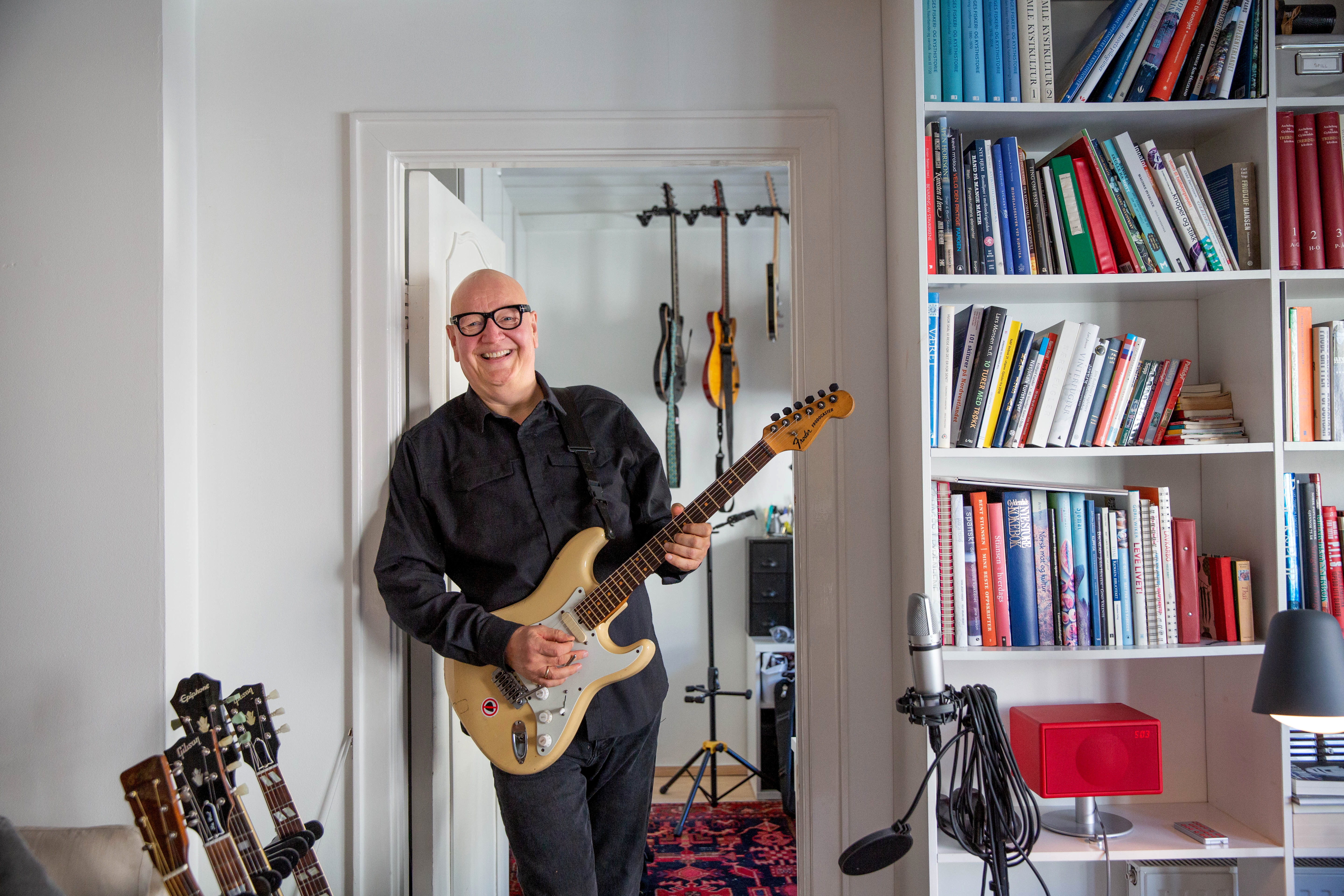 Frode Alnæs lener seg mot dørkarmen i leiligheten på Frogner og holder i gitaren