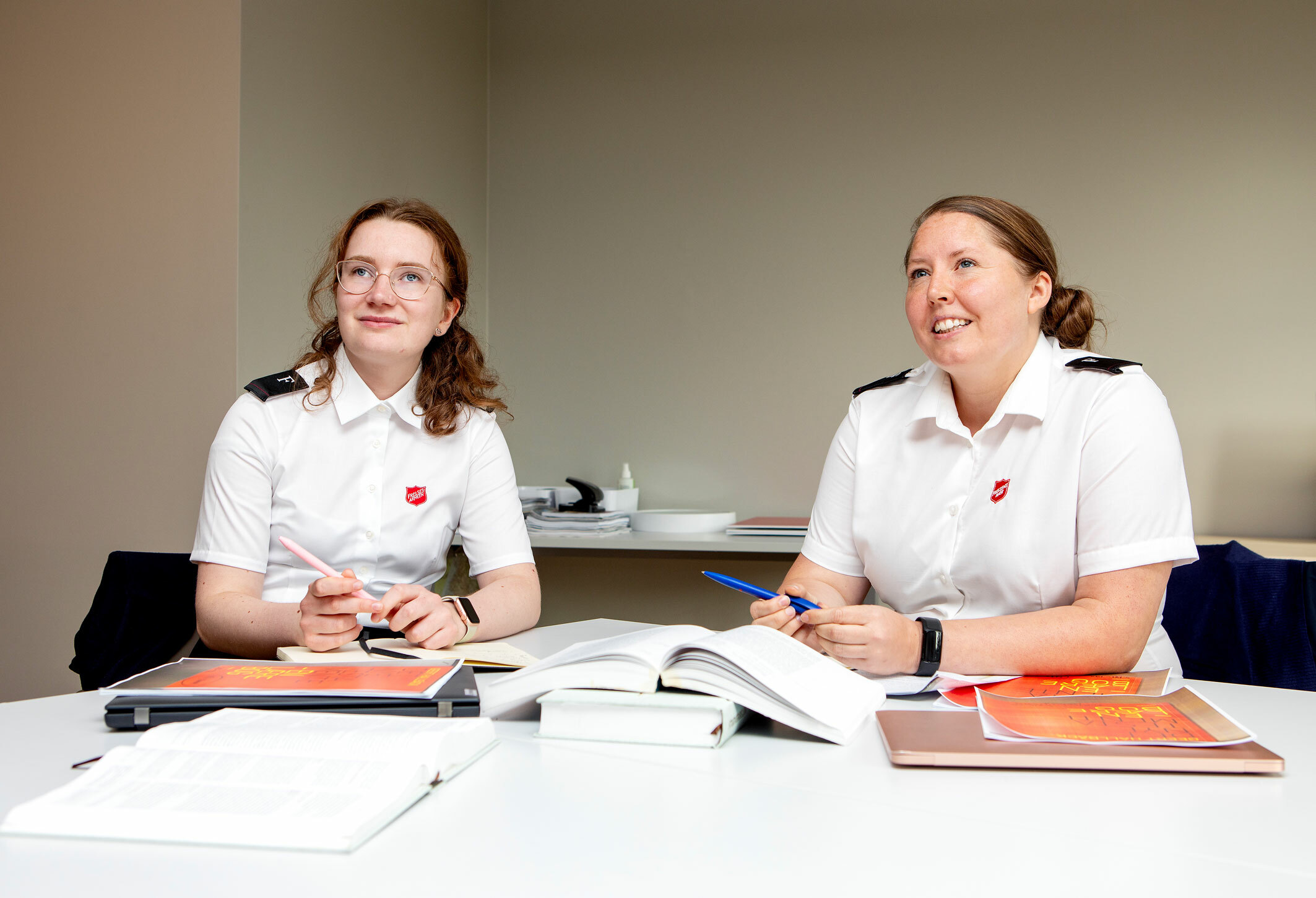 Foto: To unge kvinner, den ene med briller, sitter et klasserom med bøker foran seg. Begge har på seg uniformer fra Frelsesarmeen.