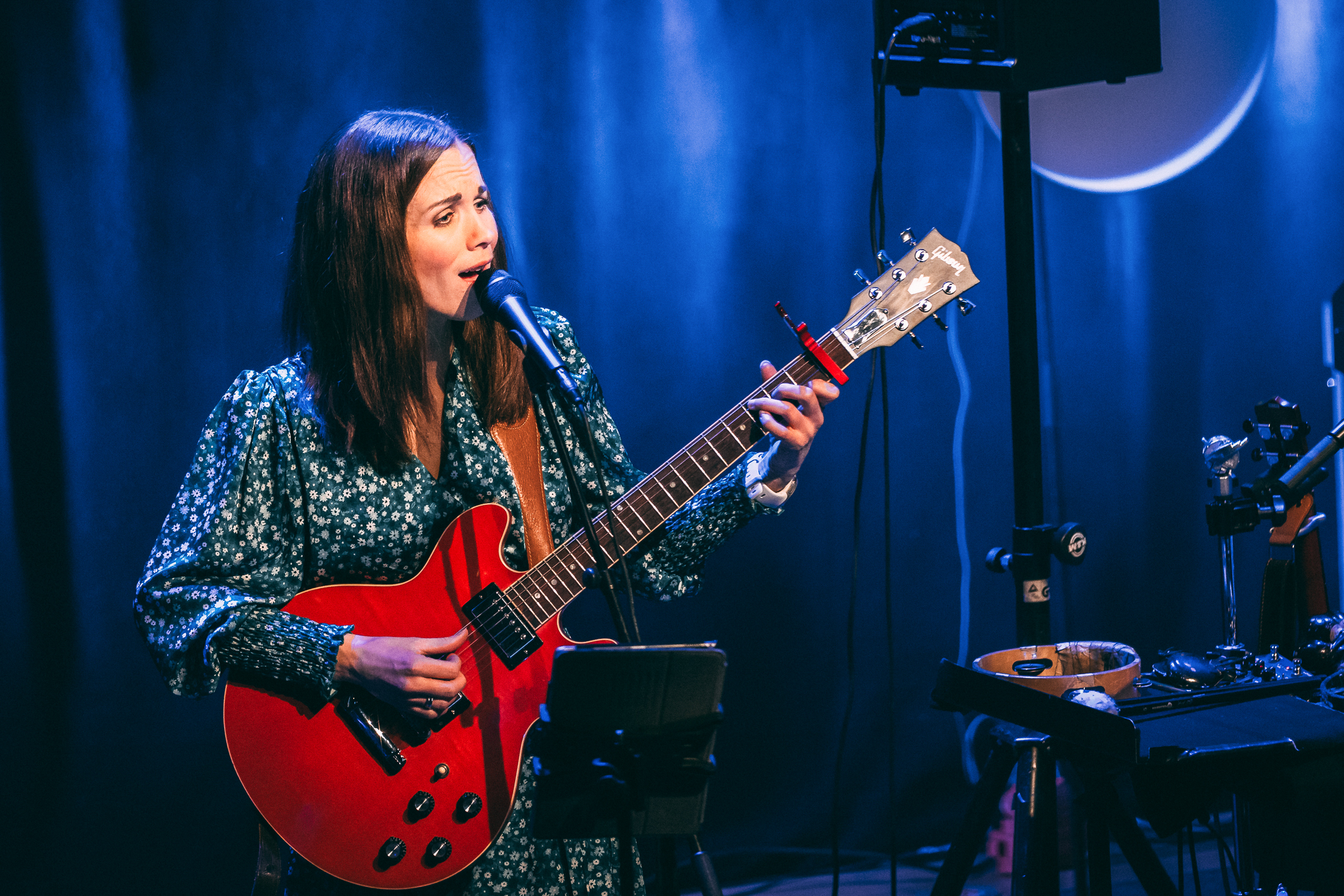 Kvinne med langt mørkt hår spiller på elgitar og synger.