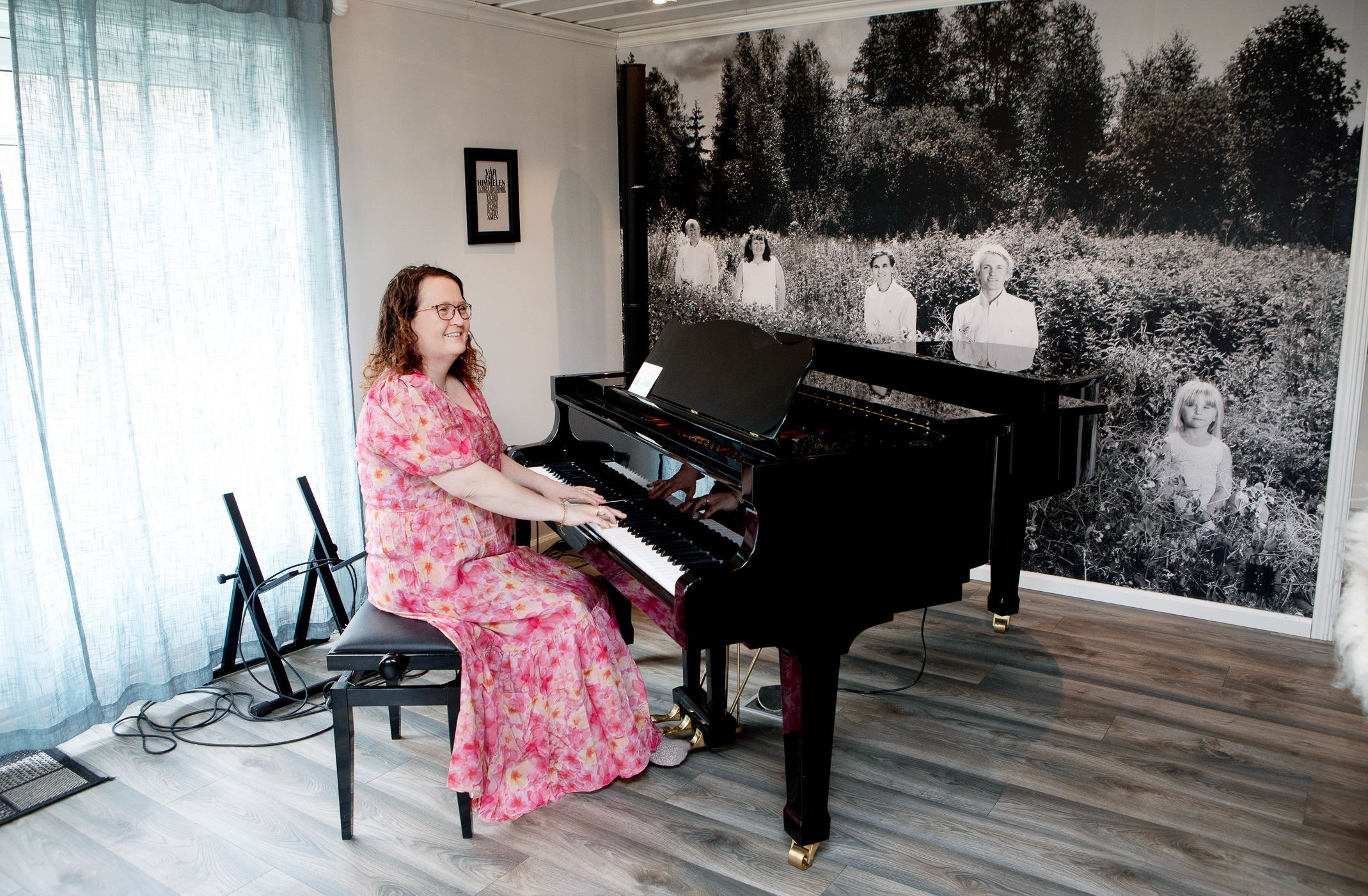 Kvinne i blomstrete kjole  spiller på et flygel i stua.