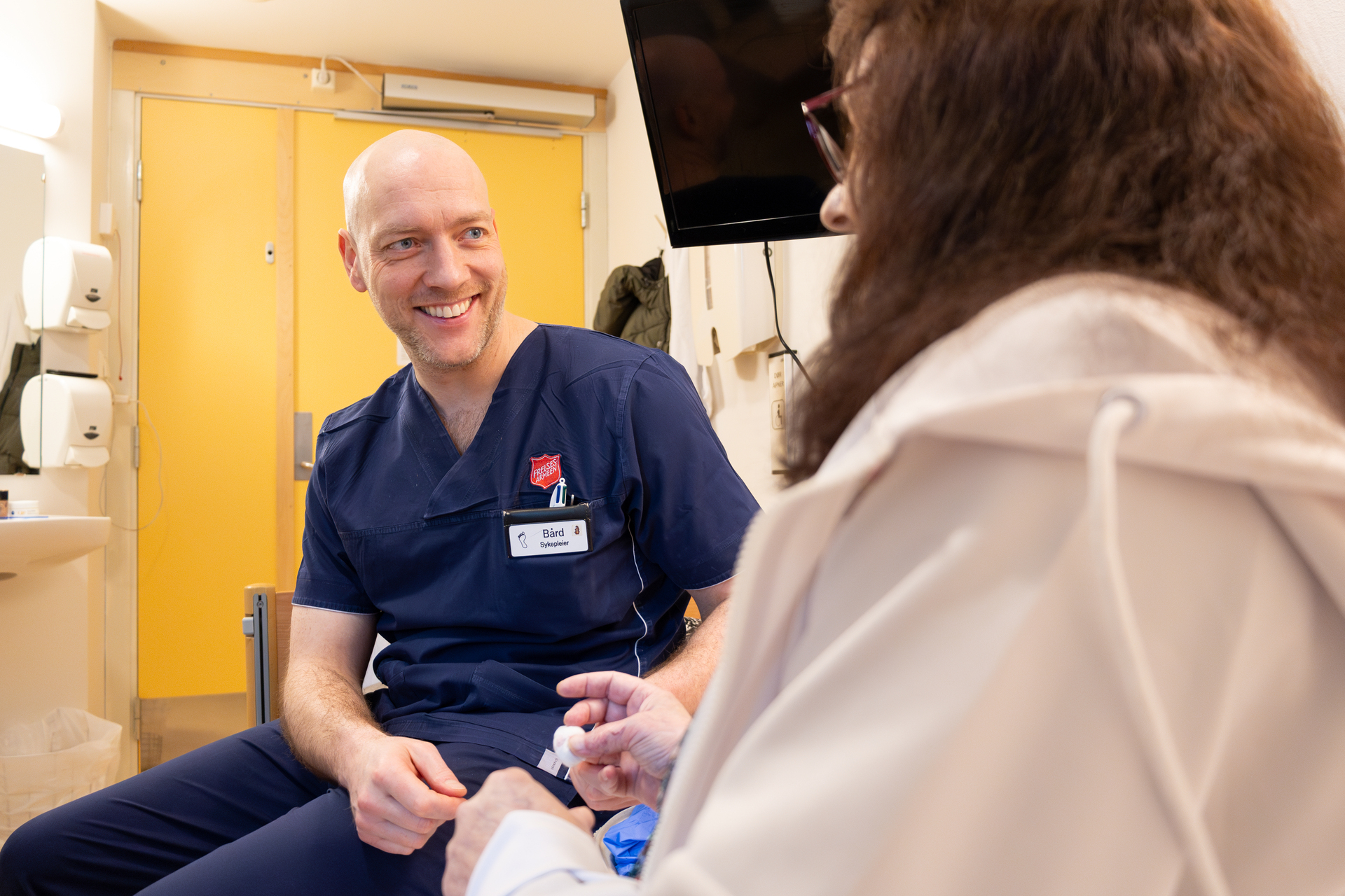 Foto: To bilder etter hverandre, der det første viser armene til en mannlig sykepleier med blå hansker som tar en blodprøve i en finger på en kvinne. Det andre bildet ham sammen med samme pasient som sitter med ryggen til kamera.