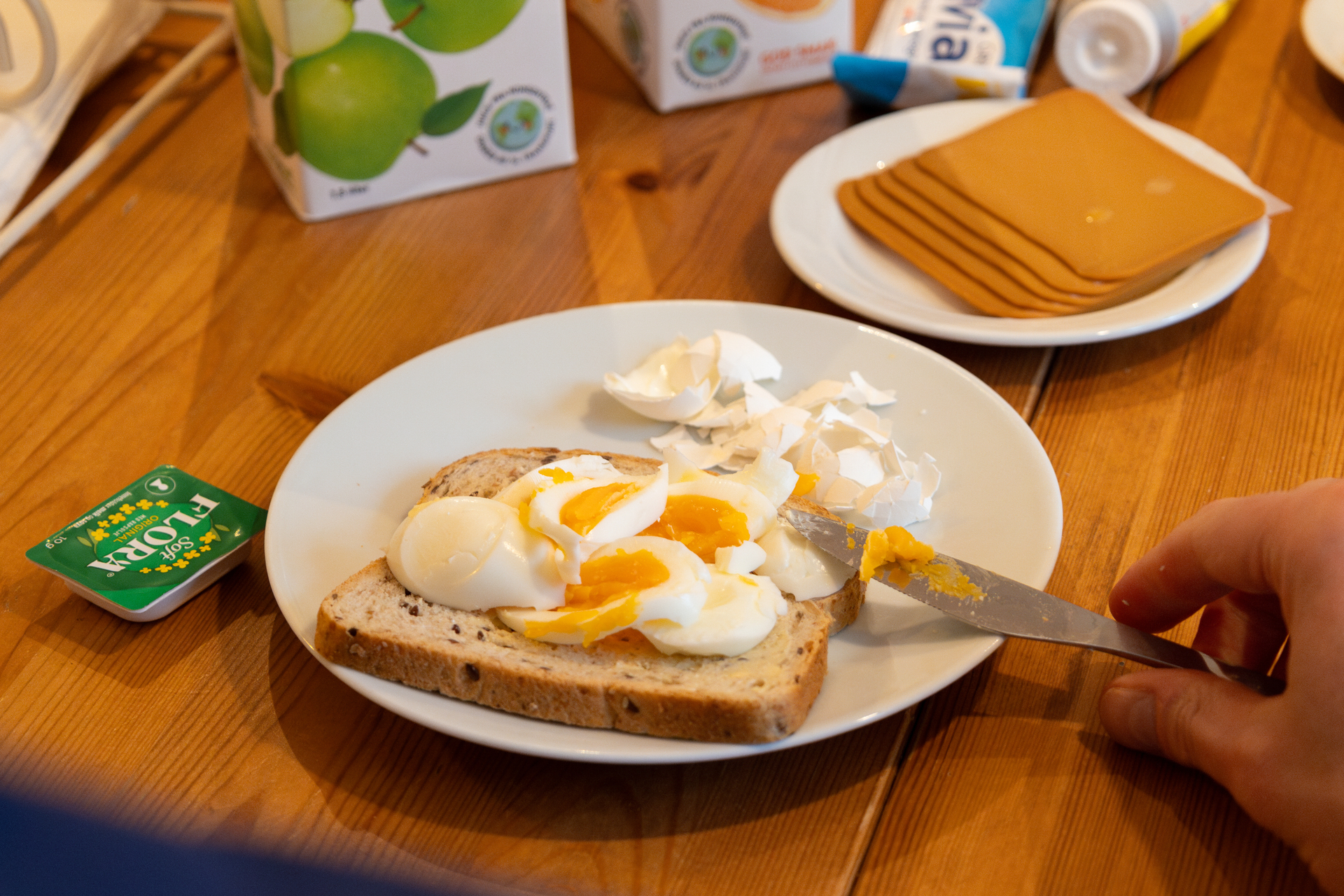 Foto: To bilder etter hverandre, der det første viser en smilende mannlig sykepleier smile. Han tar skallet av et egg ved frokostbordet, som er dekket med juice, brød og pålegg. Det andre er et nærbilde av egget som er skåret opp i biter på en brødskive.