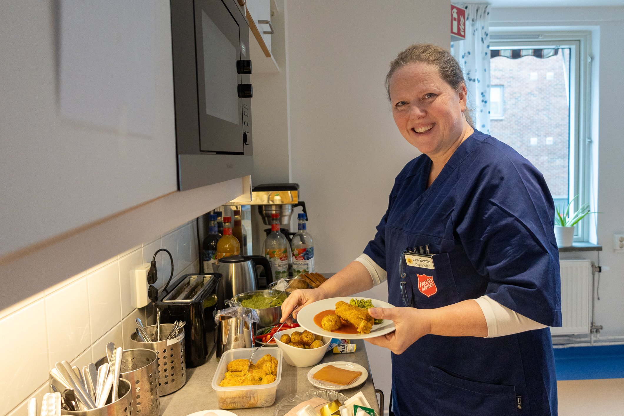 Kvinnelig sykepleier i blå uniform steller til mat på kjøkkenet.