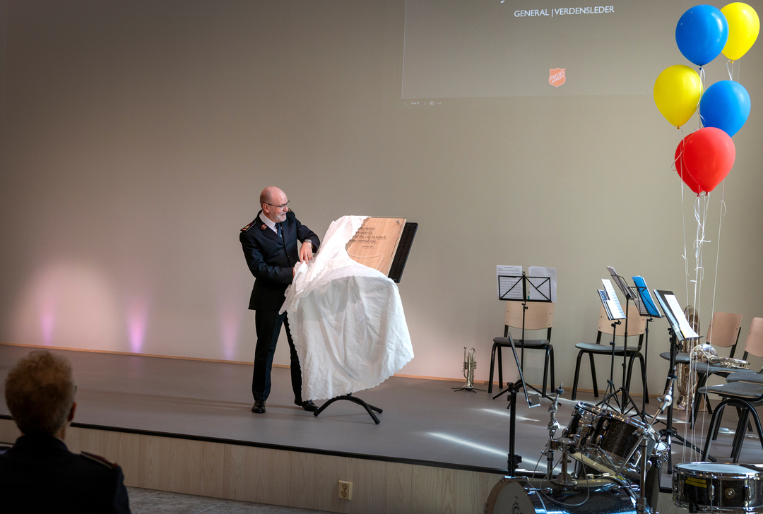 En middelaldrende mann med mørk uniform på en scene. Han drar bort et klede som dekker en plakett.