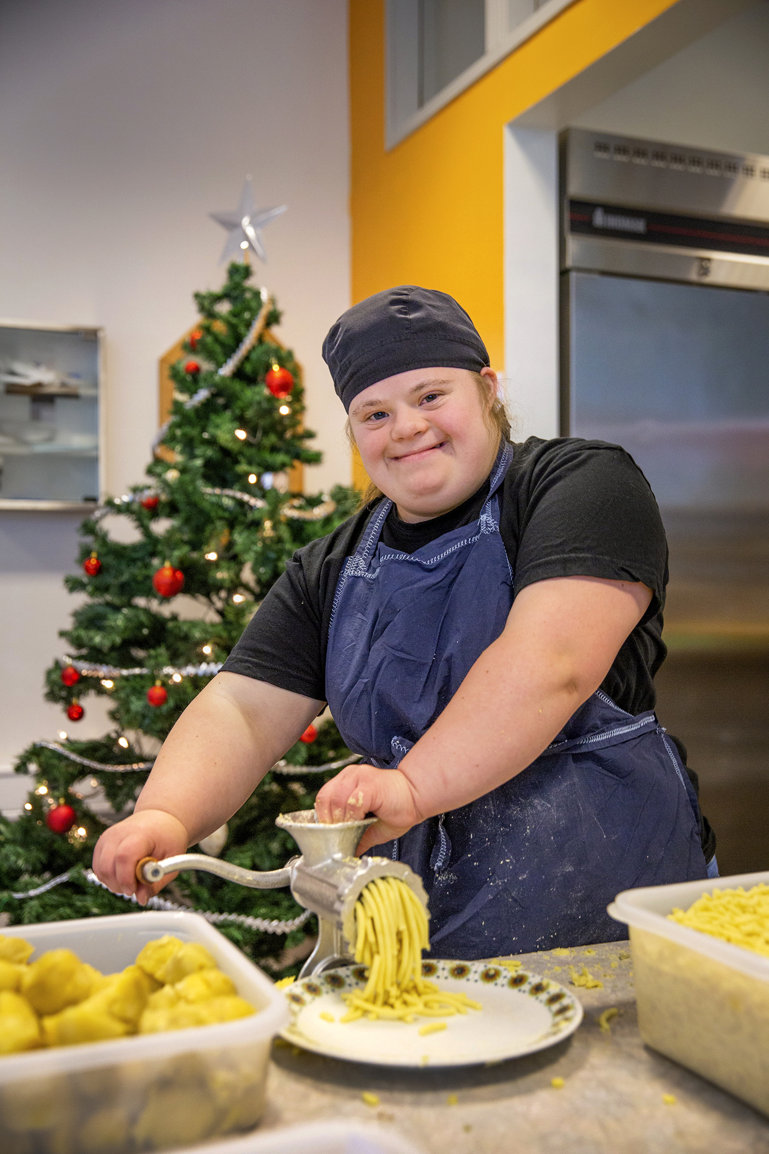 Rikke står smilende på kjøkkenet på PULS og kverner poteter - iført forkle og kokkelue.