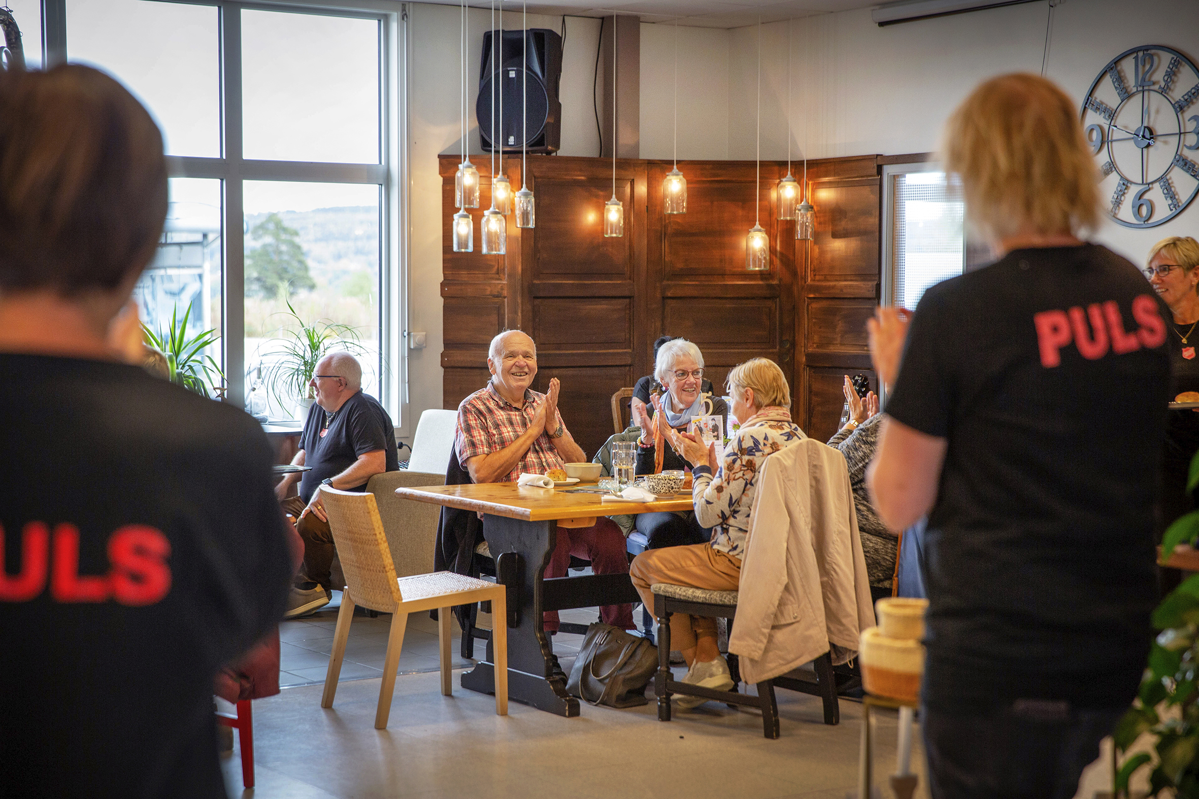 Man ser PULS-lokalet og et bord fylt med pensjonerte som koser seg på kafeen.