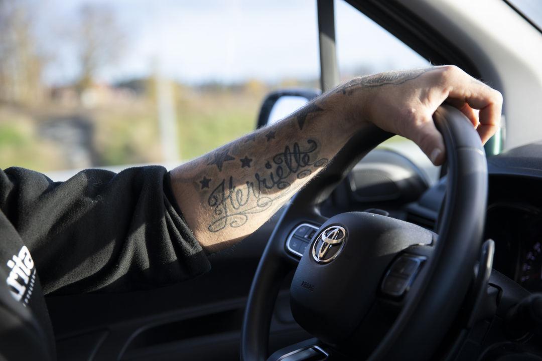 Vi ser en tatovert arm på et ratt i en bil. På armen står det Henriette.