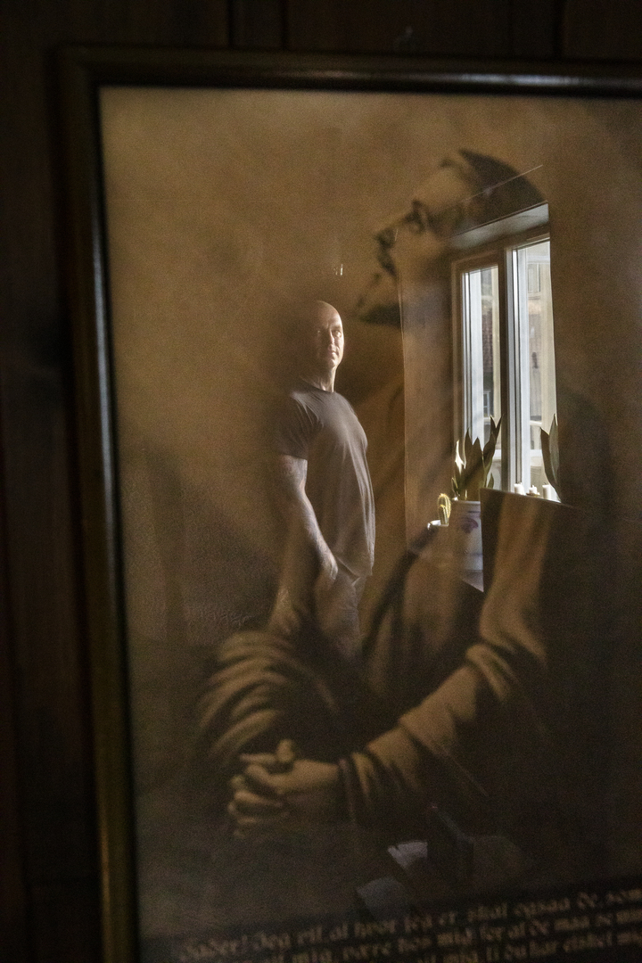 I refleksjonen i glasset på et Jesus-bilde på veggen ser vi en mann stå ved et vindu.