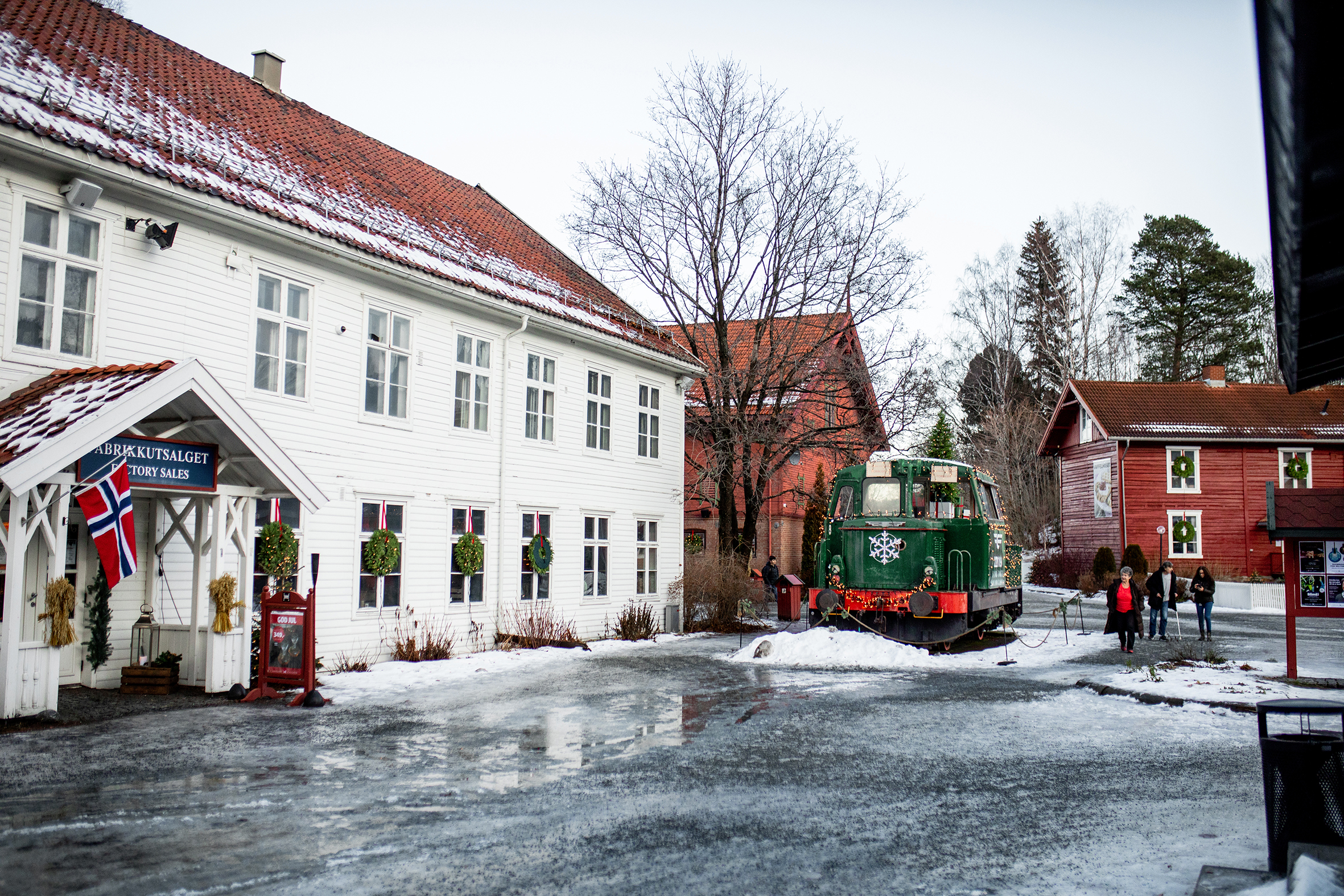 Bildet viser gamle trehus i rødt og hvitt, med kranser og annen julepynt og et norsk flagg.