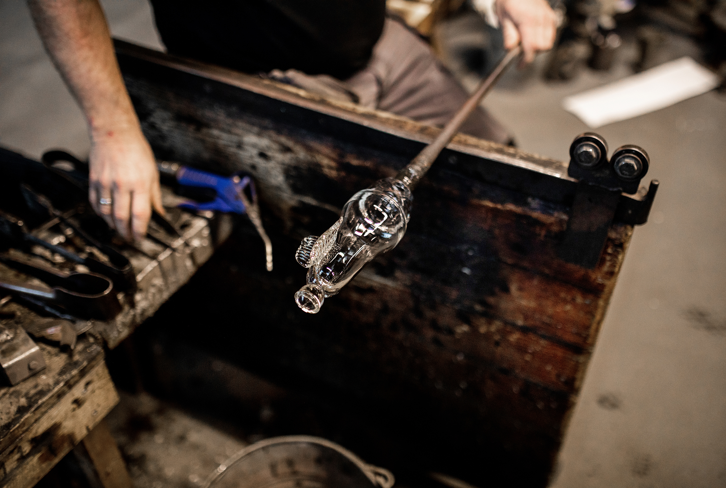 Bildet viser to menn som står og holder hver sin metallstang med oppvarmet glass på.