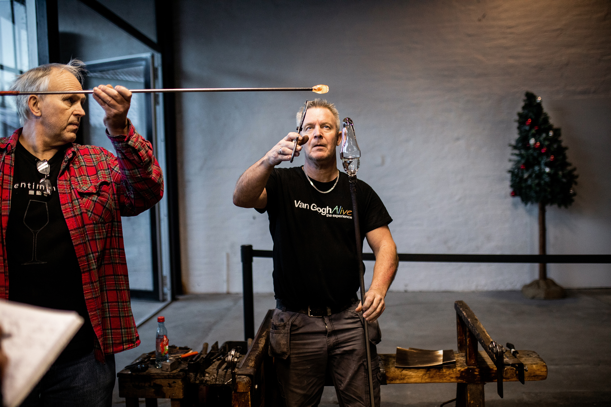 Bildet viser to menn som står og holder hver sin metallstang med oppvarmet glass på.