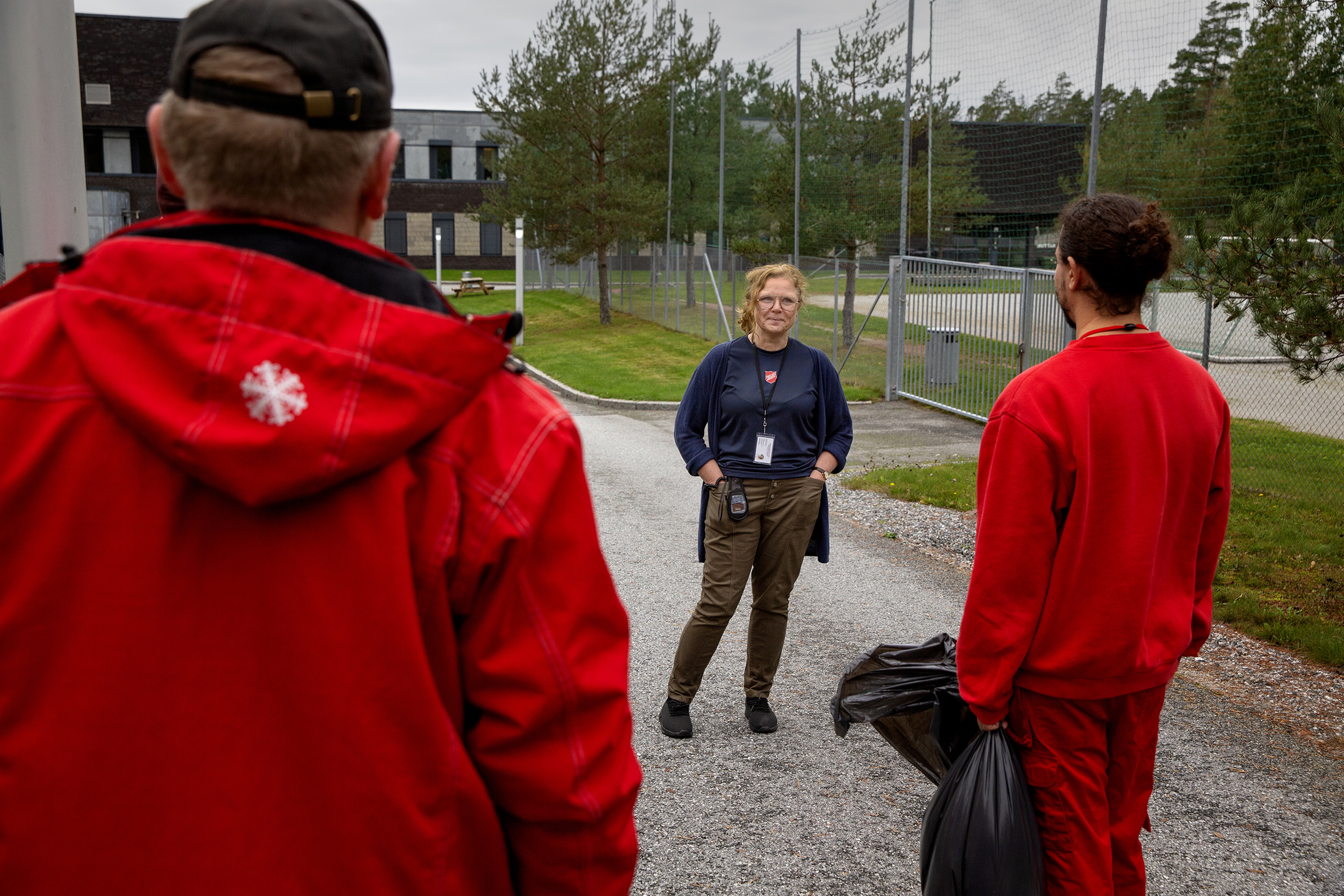 Marit Skartveit snakker med to innsatte i røde fengselsdrakter, innen for murene i Halden fengsel