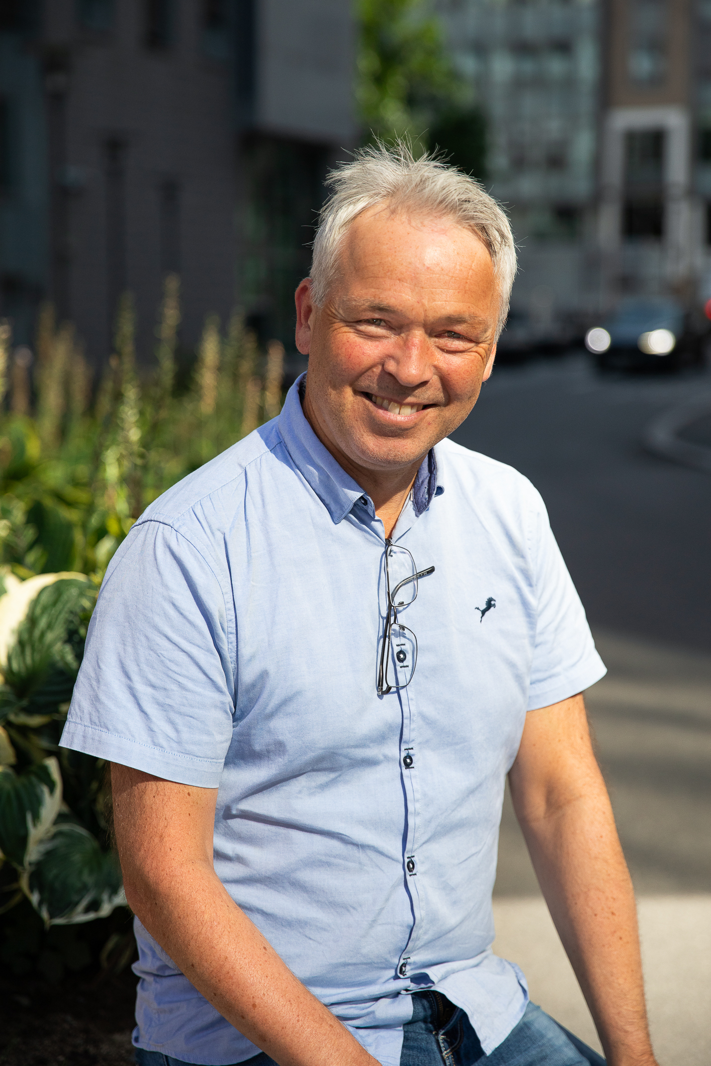 Solbrun mann i blå, kortermet skjorte smiler i sollyset utendørs. Høydebilde.