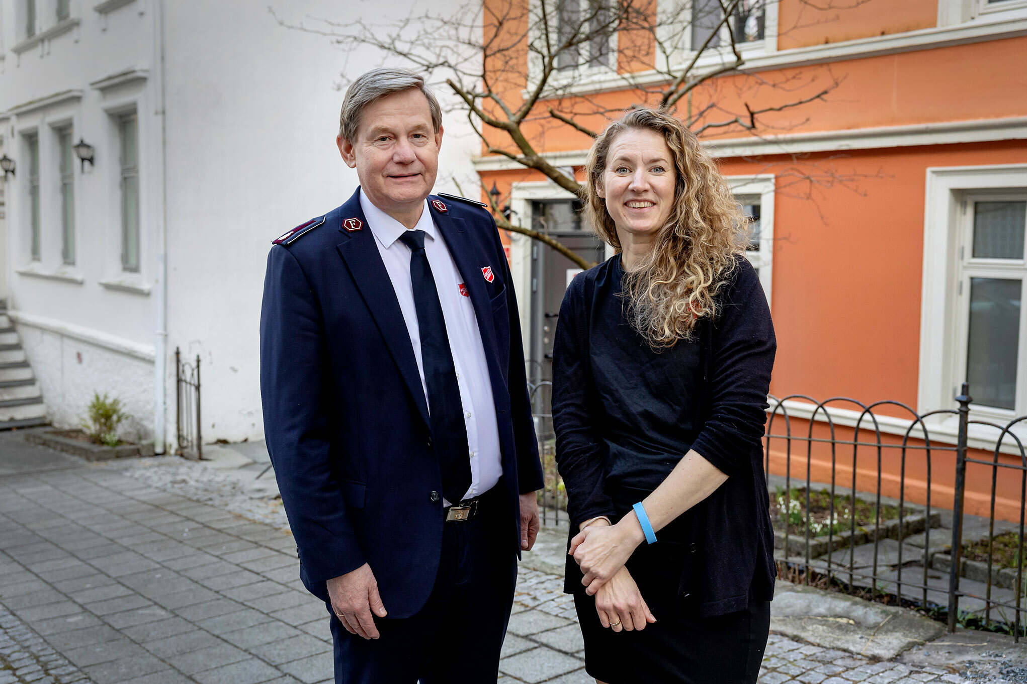 Foto: Mann i uniform fra Frelsesarmeen og kvinne med langt, krøllete hår står utenfor en  gammel murbygning.