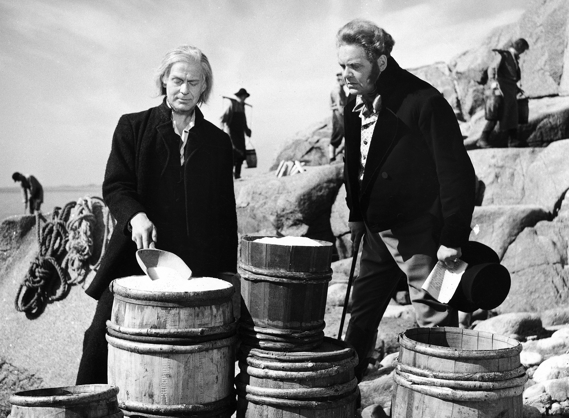 Sort/hvitt bilde fra filmen «Hans Nielsen Hauge», 1960. (Foto: NTB) Hauge og en annen mann står blandt tønner i skjærgården.