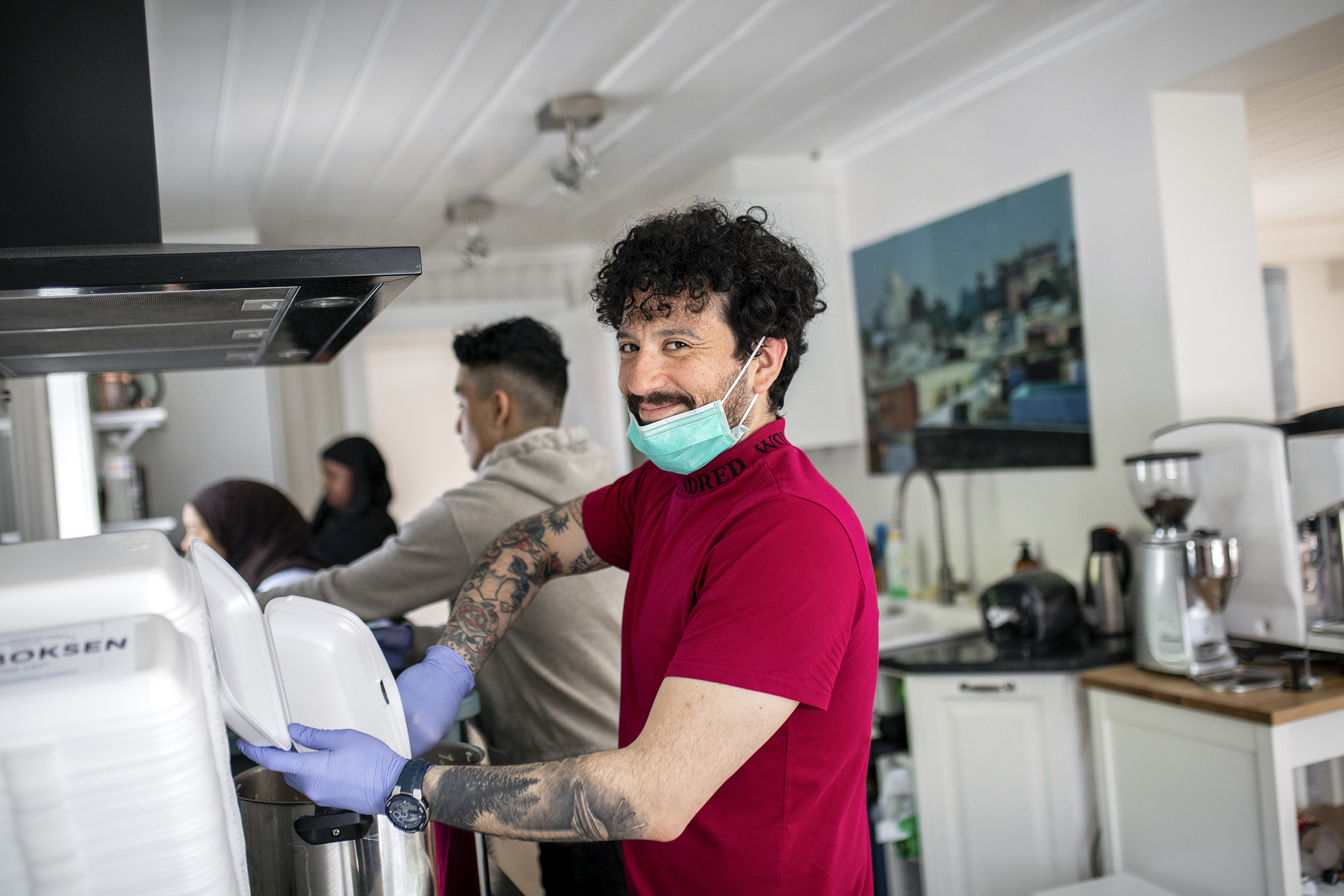 Felipe Castro arbeider på kjøkkenet. Han har dratt ned munnbindet og smiler til kameraet mens han pakker middag ned i en take away-boks.