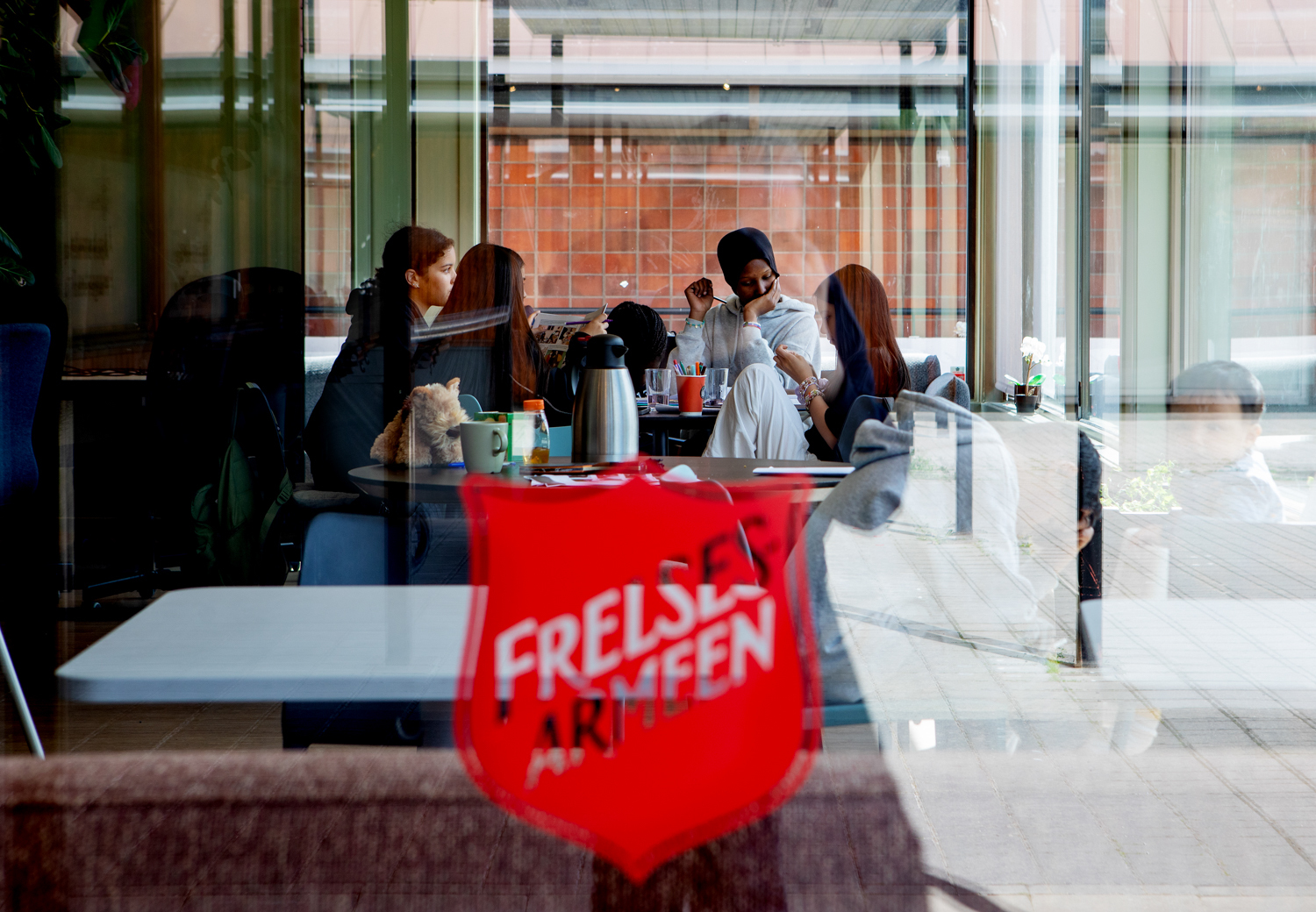 Foto: Bildet viser korpsets lokaler tatt utenfra. Det er et stort Frelsesarme-skjold på vinduet, og inne skimtes en gjeng med barn som sitter rundt et bord.