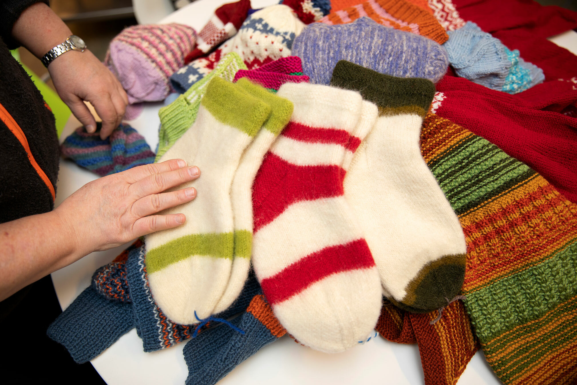 Foto: Et par hender fra en kvinne, med klokke på venstre armen, inspiserer mange par med hjemmestrikkede sokker.