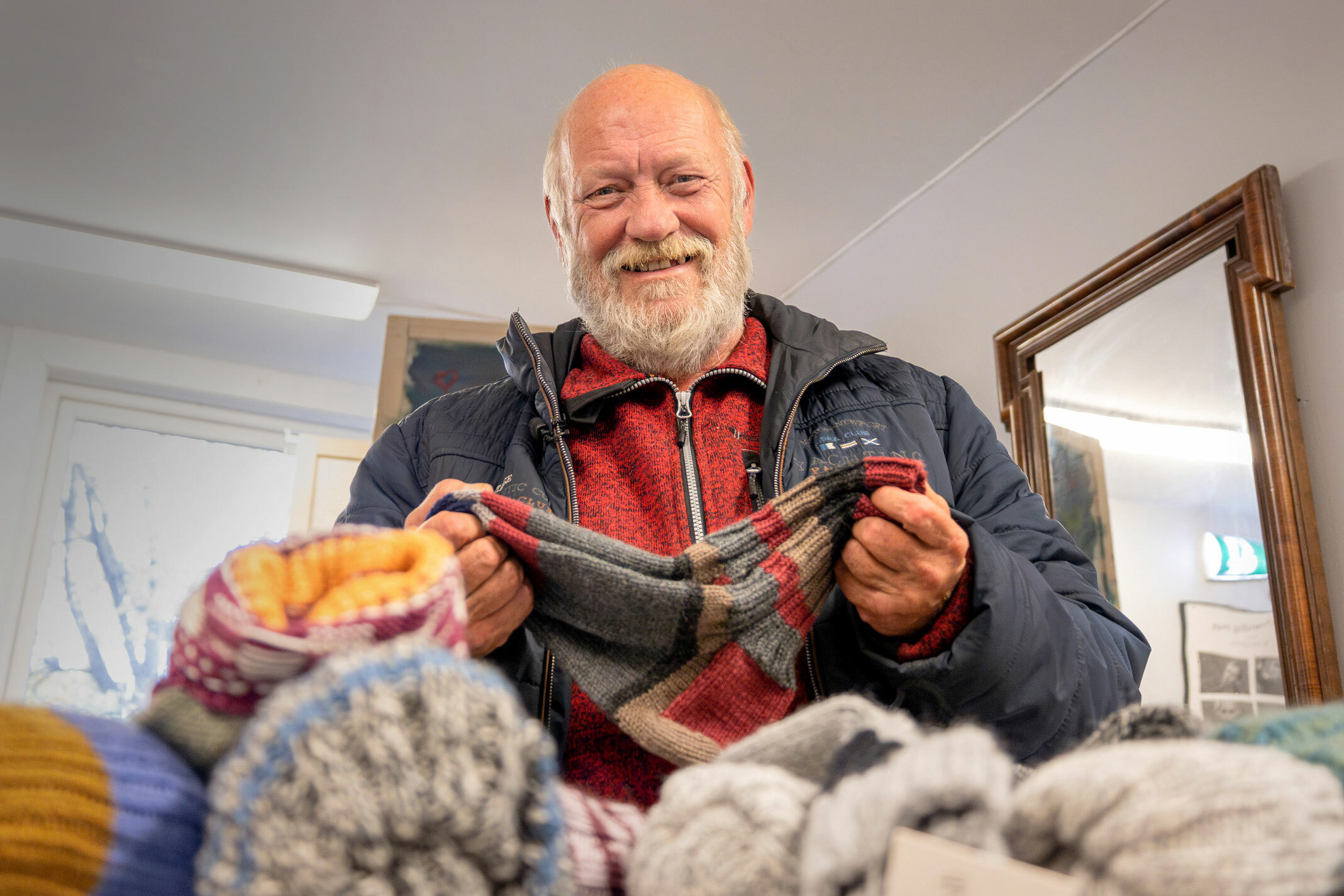Foto: Gammel mann holder et par hjemmestrikkede ullsokker mellom hendene. Foran ham ligger et berg av strømpepar.