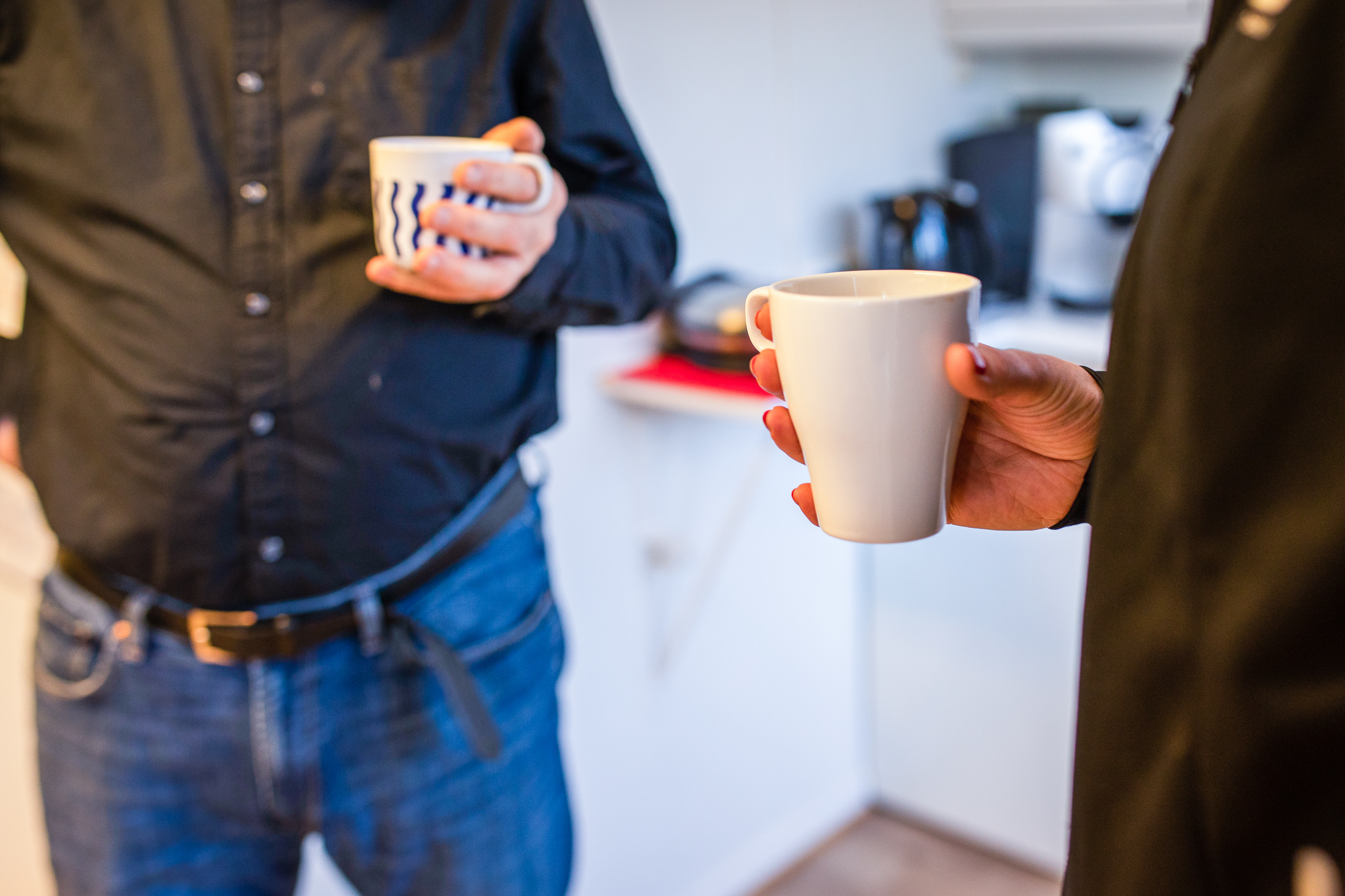 En mann og en dame står med hver sin kaffekopp. Bildet er anonymisert og uten hoder